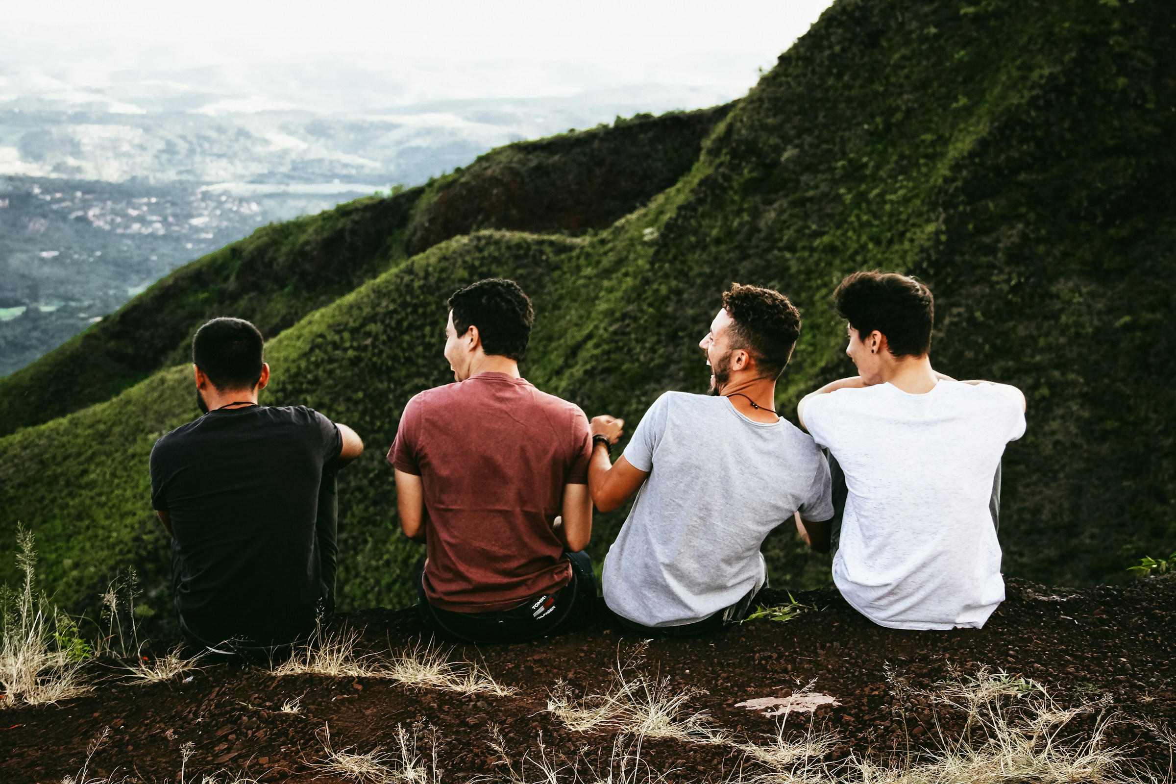 Vier junge Männer sitzen auf einem Bergpfad | Quelle: Unsplash