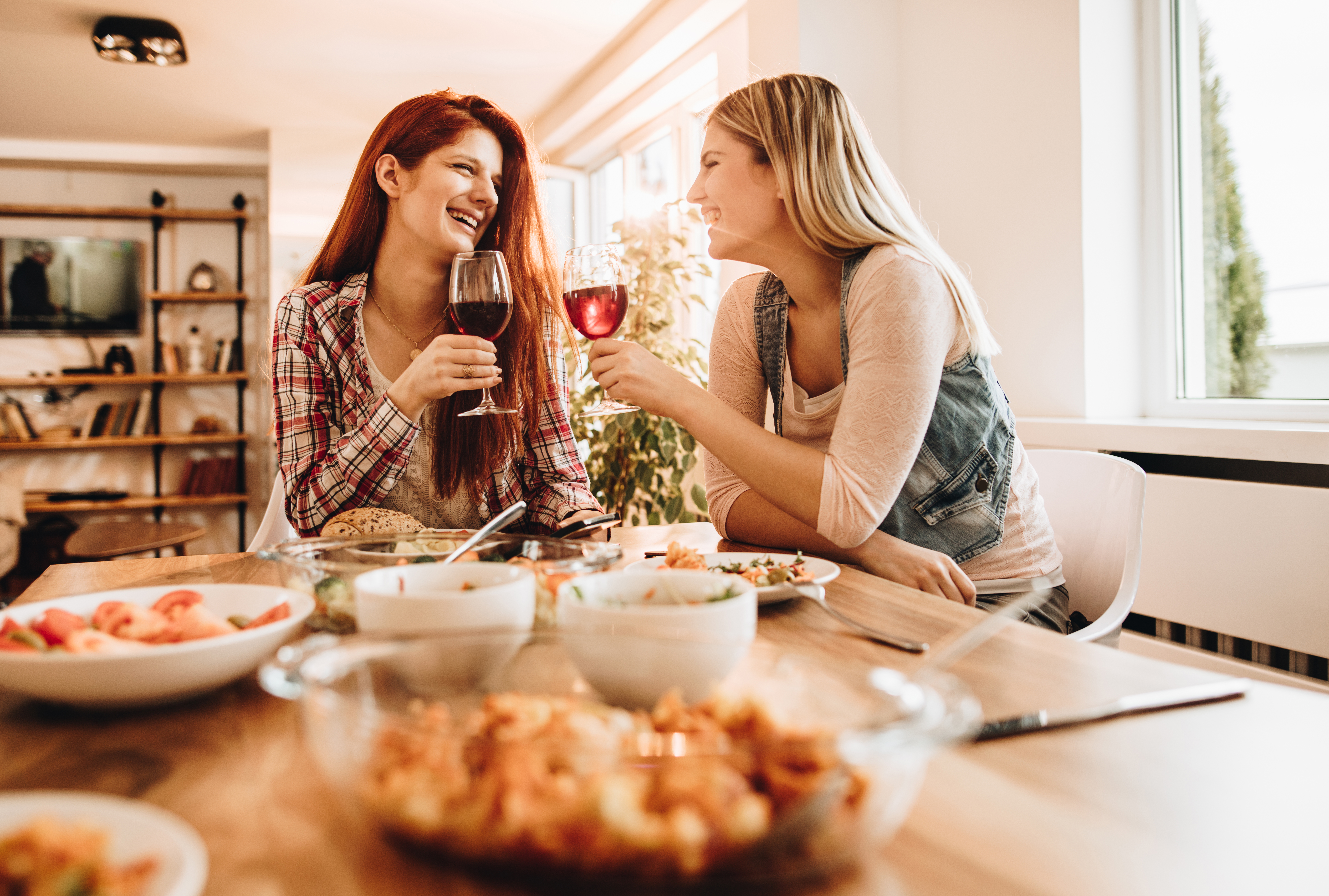Junge glückliche Frauen, die sich beim Mittagessen unterhalten und Wein trinken | Quelle: Getty Images