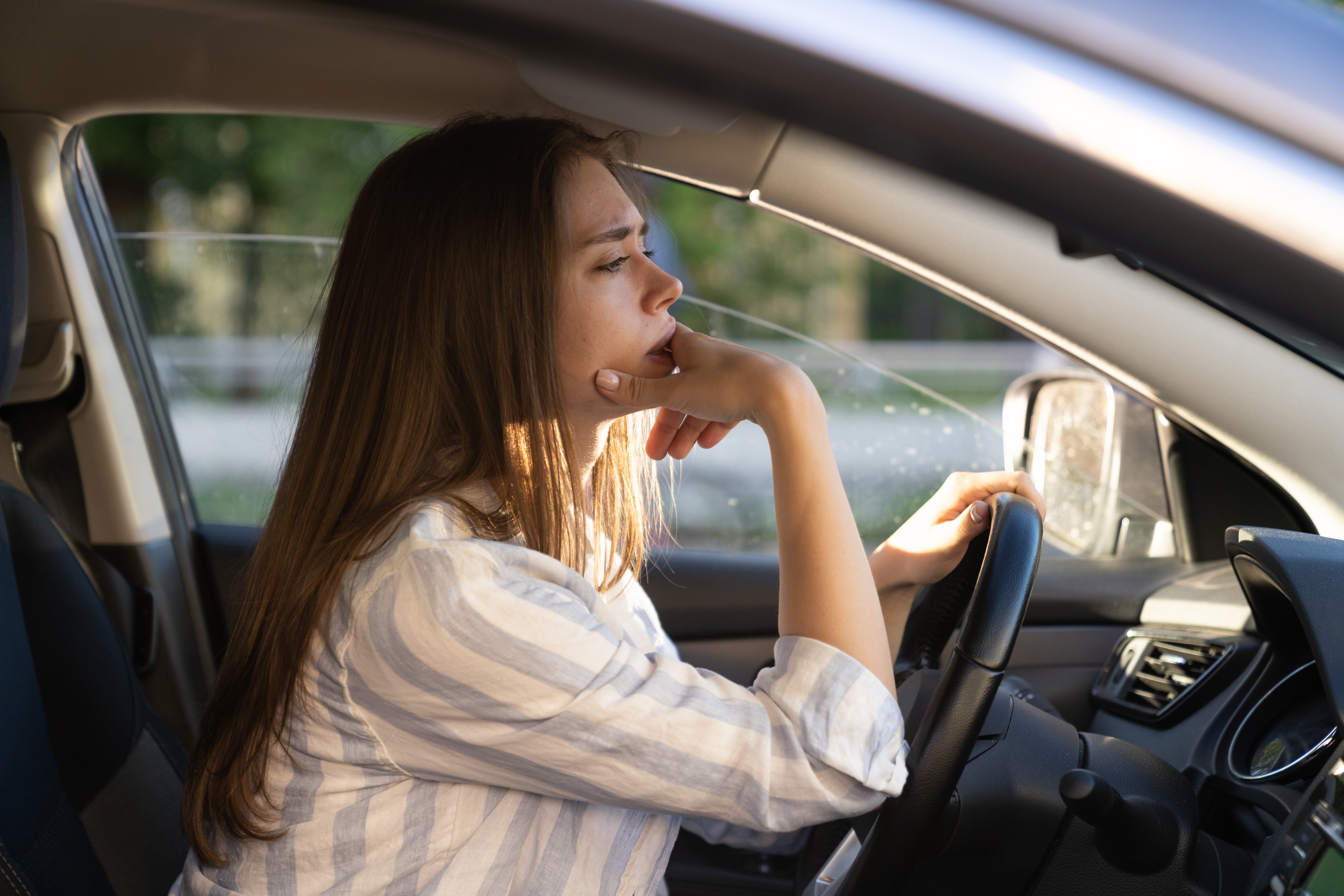 Eine traurige, müde junge Frau am Steuer eines Autos | Quelle: Shutterstock