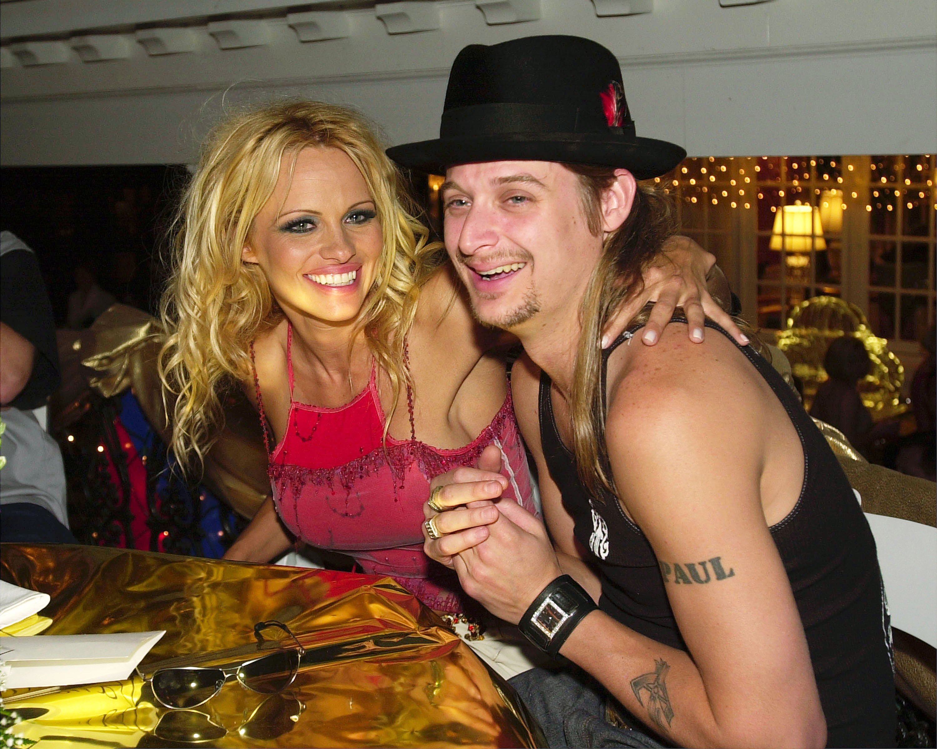 Pamela Anderson und der Musiker Kid Rock lachen gemeinsam, während sie sich am 4. Mai 2001 bei der Barnstable-Brown Derby Eve Gala in Louisville, Kentucky, auf ihre Plätze setzen. Anderson trägt ein besticktes magentafarbenes Oberteil, ihre Sonnenbrille liegt auf dem goldverzierten Tisch. Sie legt einen Arm um Rock und fängt so das energiegeladene Rampenlicht ihrer Beziehungen aus den frühen 2000er Jahren ein, bevor sie die Spektakel auf dem roten Teppich gegen die ruhige Zweisamkeit in Arcady eintauschte. | Quelle: Getty Images
