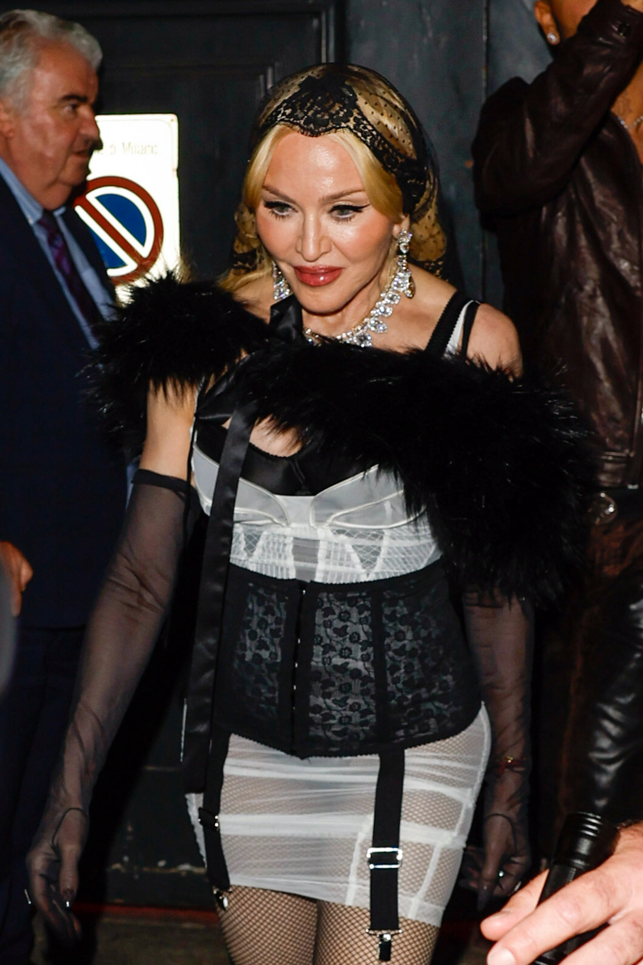 Madonna verlässt am 21. September 2024 eine Dolce & Gabbana-After-Party in Mailand. Sie trug ein schwarz-weißes Outfit mit durchsichtigen Handschuhen, Federdekorationen, mit Edelsteinen besetzten Accessoires und einer schwarzen Spitzenkopfbedeckung. | Quelle: Getty Images
