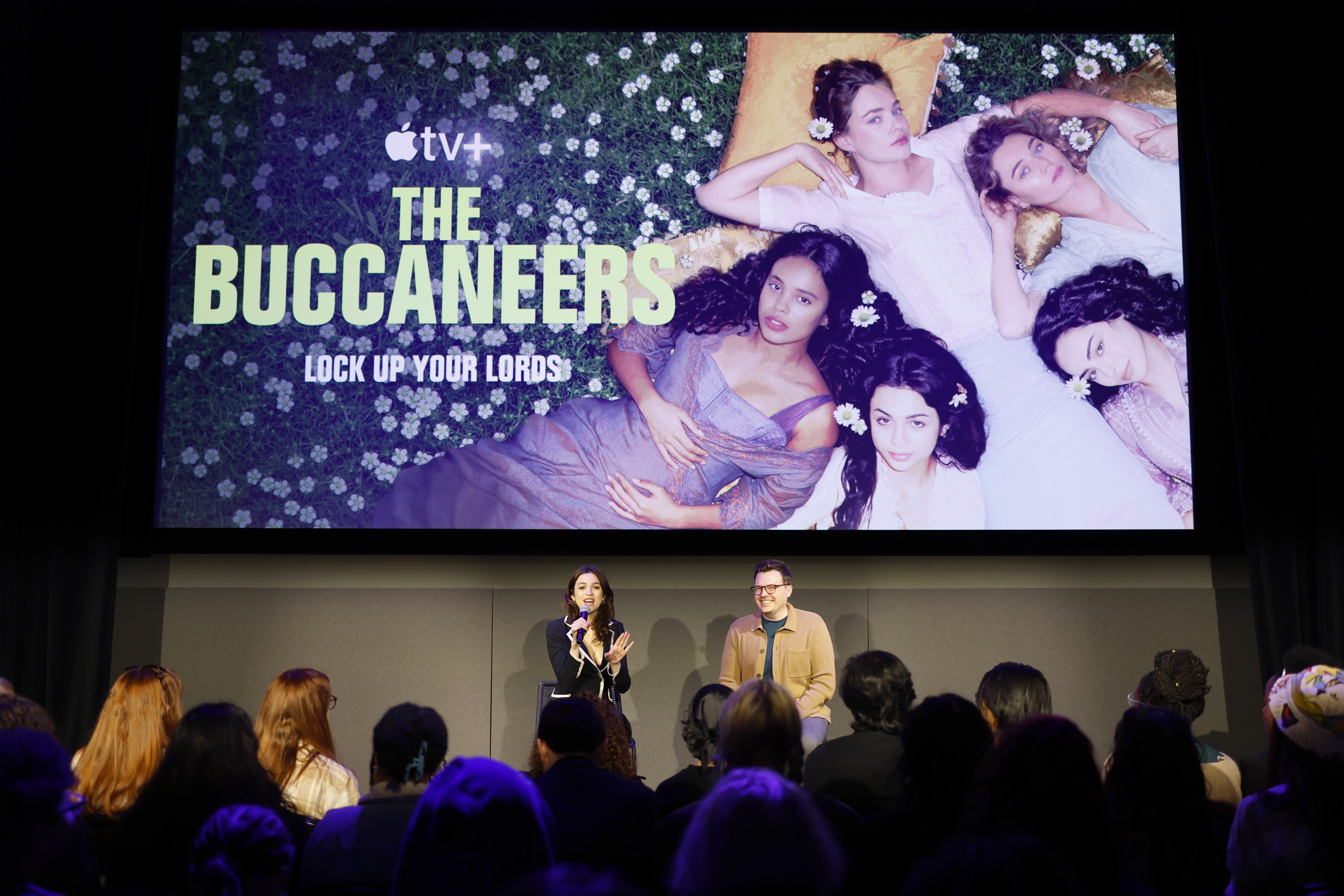 Josie Totah spricht am zweiten Tag des 12. SCAD TVfest während der Podiumsdiskussion zu „The Buccaneers“ und sitzt dabei auf der Bühne neben einem anderen Diskussionsteilnehmer, während sie sich an das Publikum wenden. Auf dem Bildschirm hinter ihnen ist ein großes Werbebild für die Apple TV+-Serie zu sehen. | Quelle: Getty Images