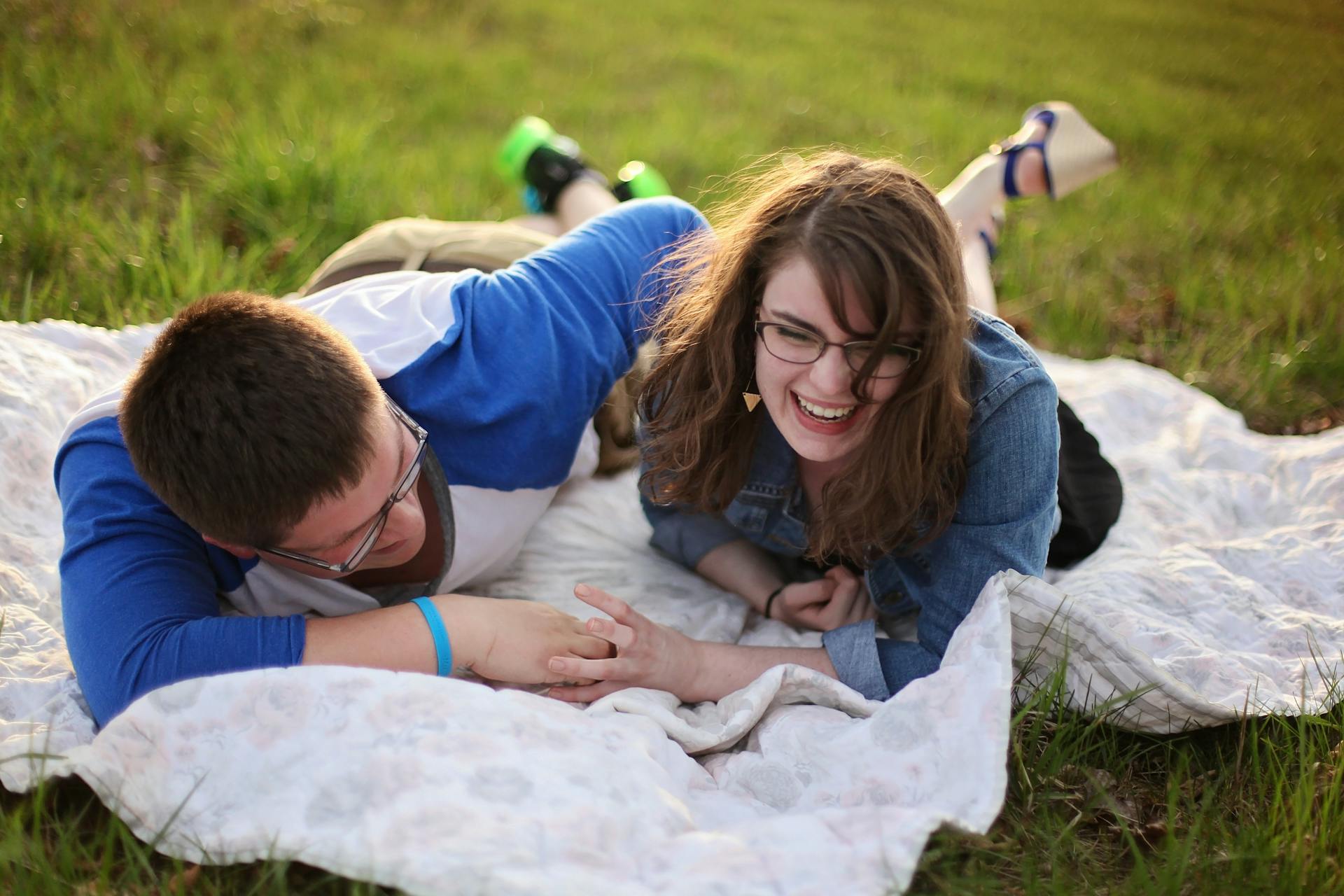 Ein Mann und eine Frau lachen, während sie auf einer Matte im Gras liegen | Quelle: Pexels