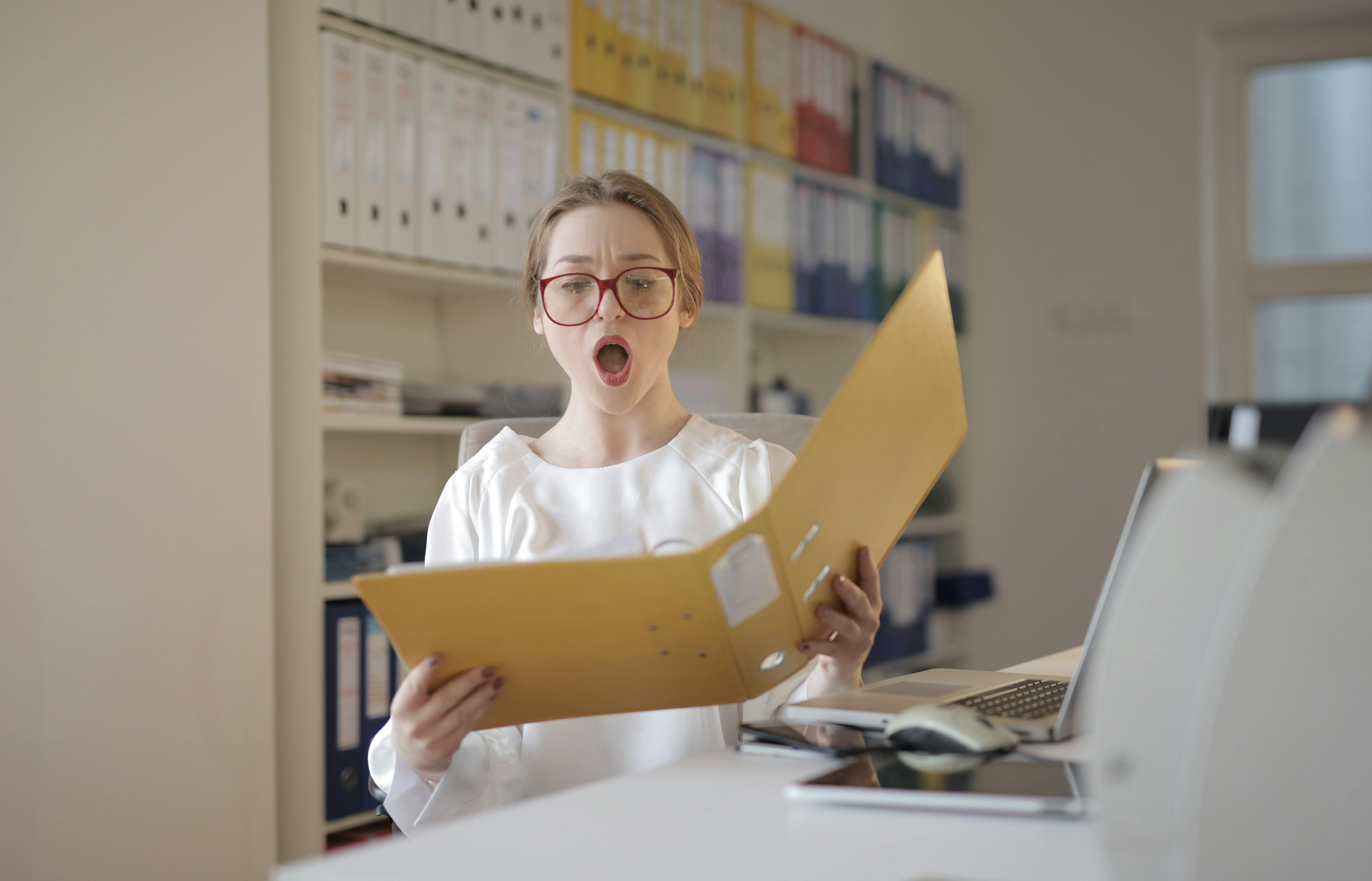 Eine Frau reagiert geschockt auf Papierkram in einem Aktenordner | Quelle: Pexels