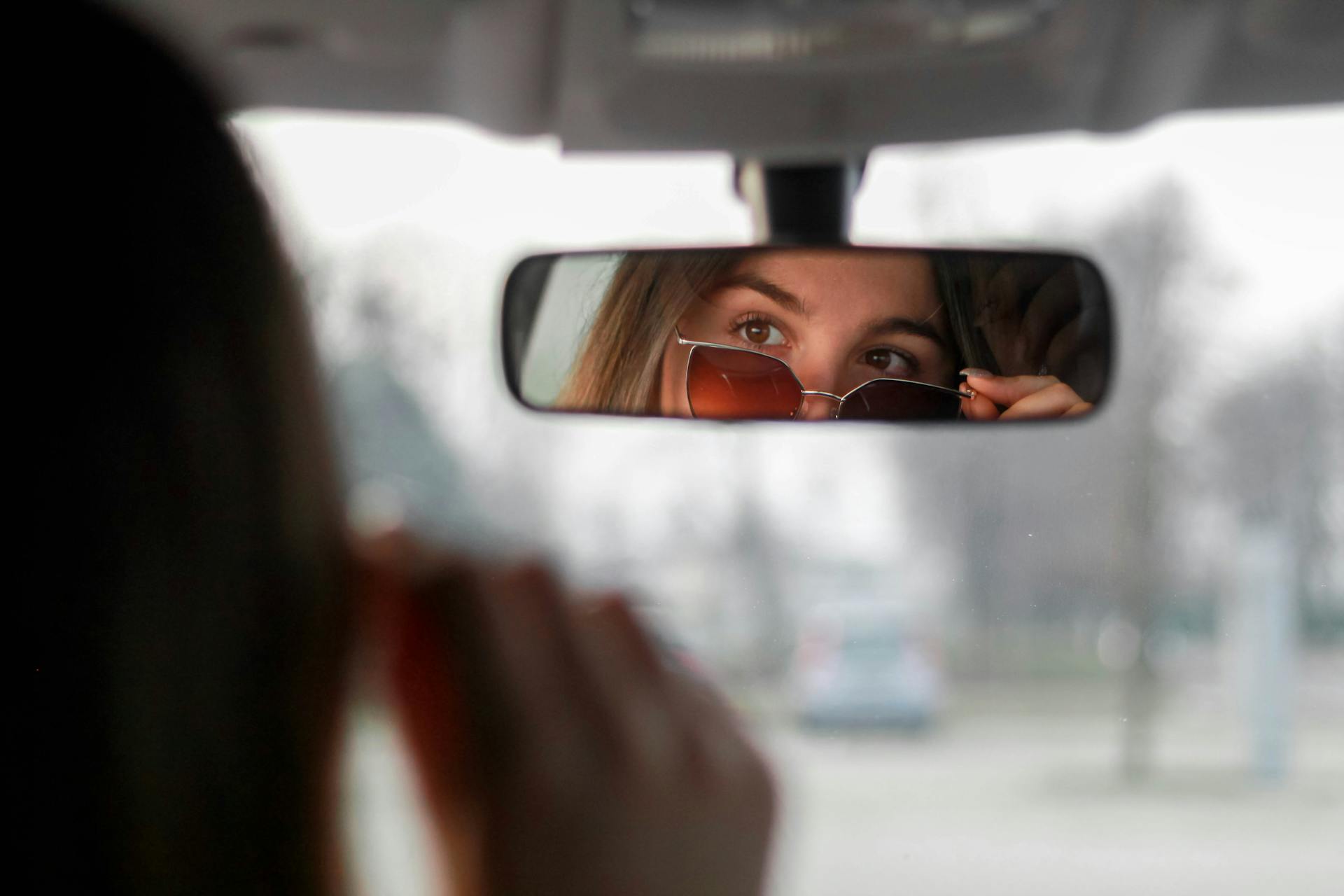 Selbstbewusste Frau mit Sonnenbrille, die ihr Spiegelbild im Rückspiegel betrachtet | Quelle: Pexels