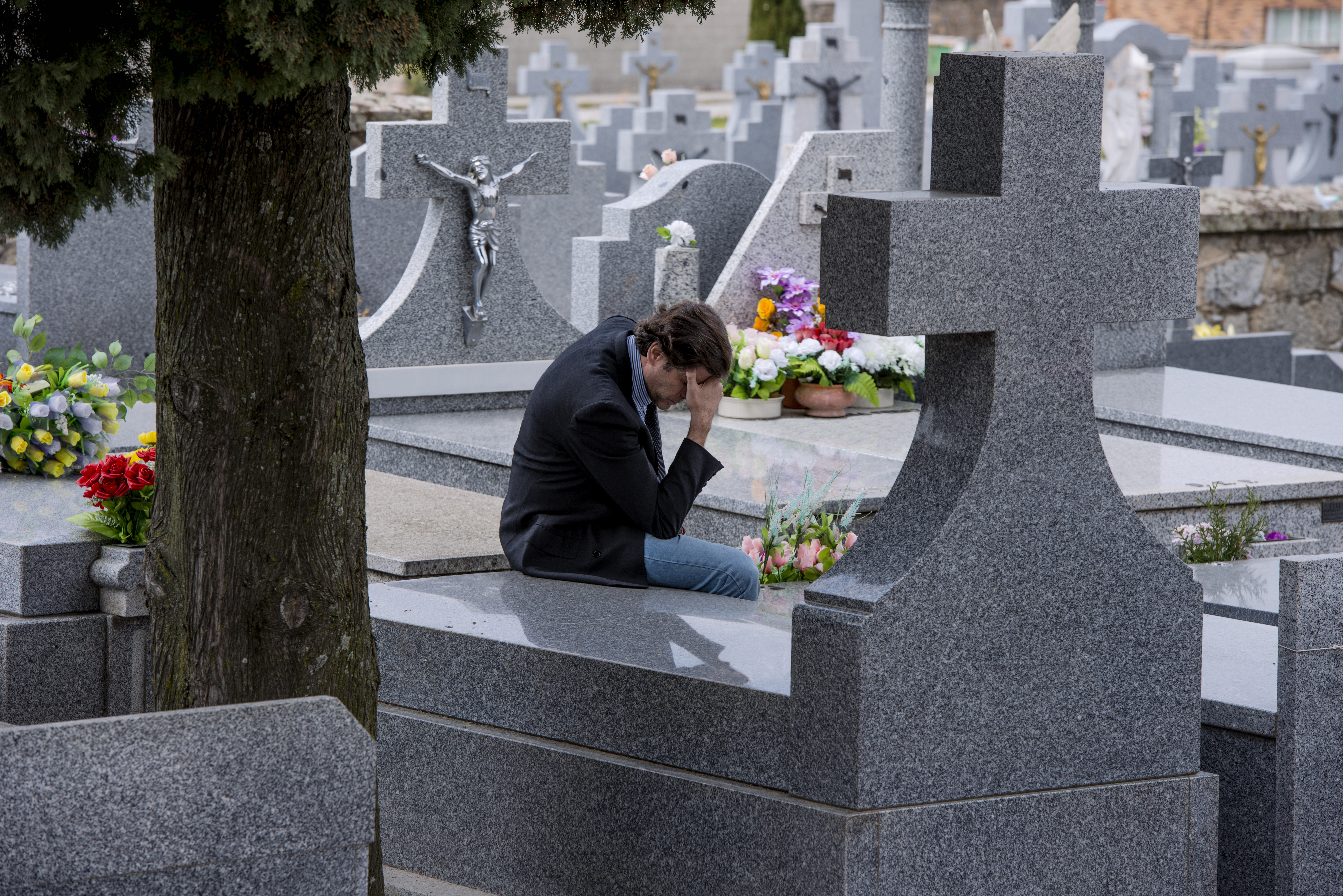 Ein am Boden zerstörter Mann sitzt auf einem Friedhof | Quelle: Shutterstock