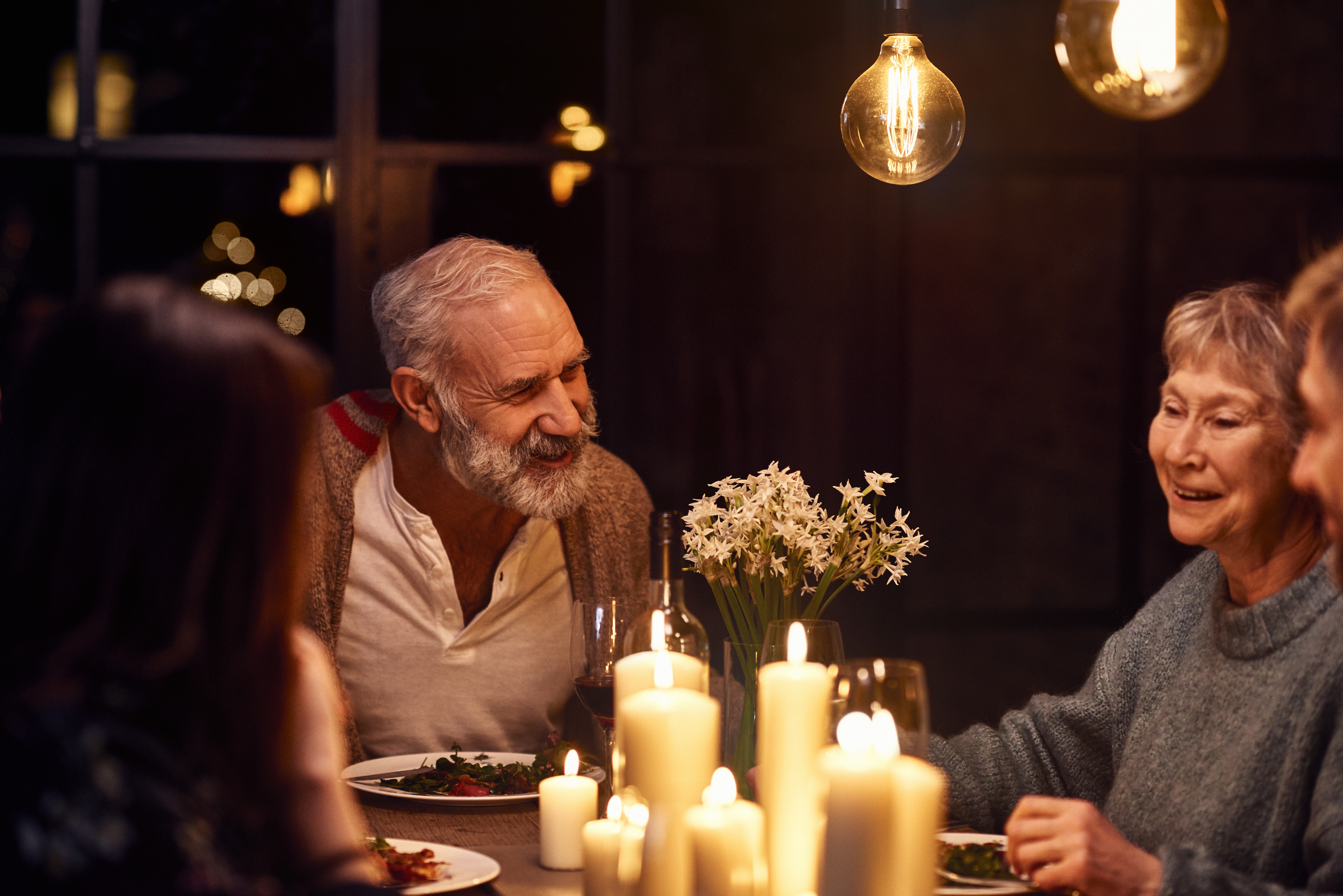 Älterer Mann, der sich auf einer Dinnerparty unterhält und mit seiner Familie lächelt | Quelle: Getty Images
