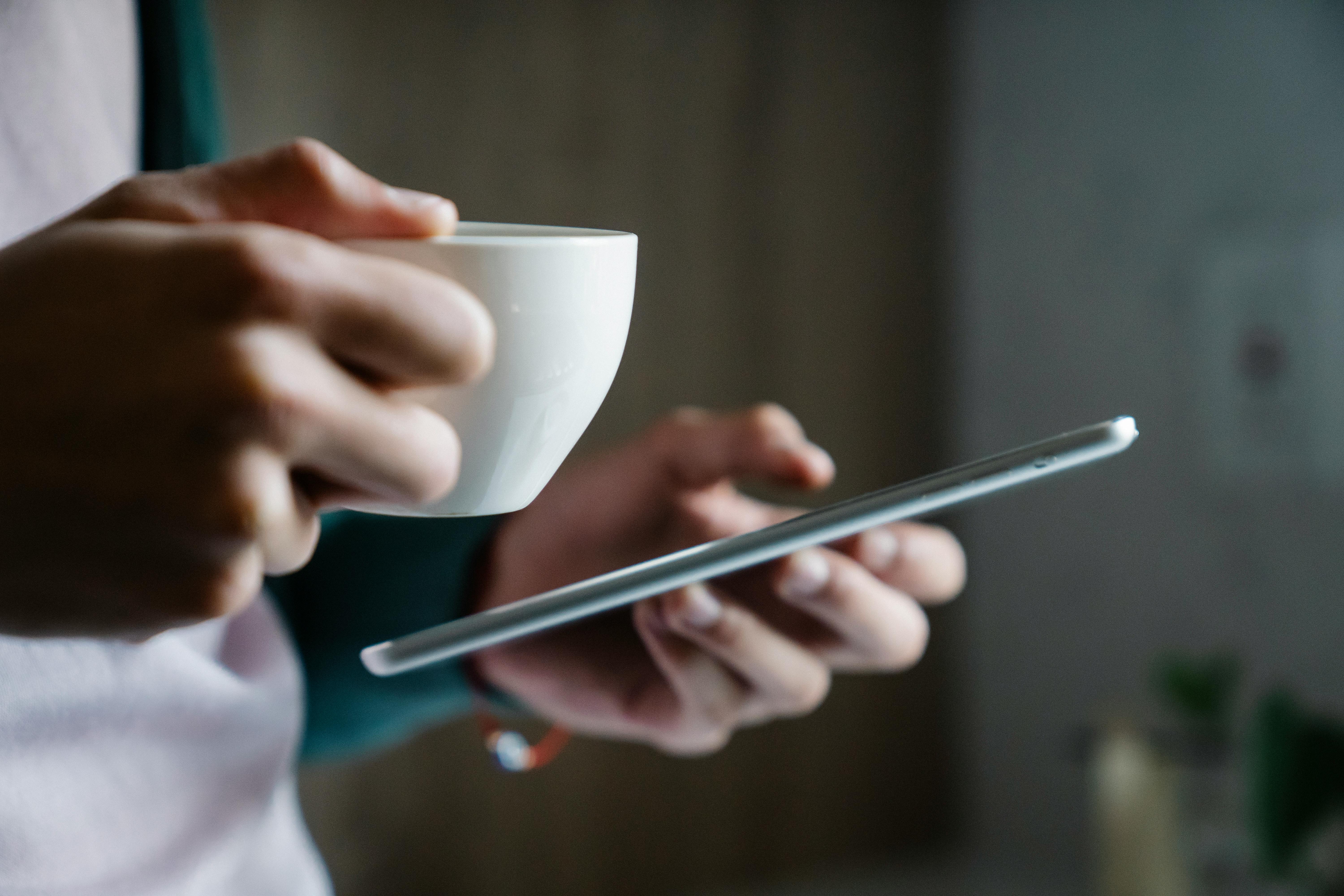 Nahaufnahme einer Person mit einer Tasse Kaffee und einem Smartphone | Quelle: Pexels