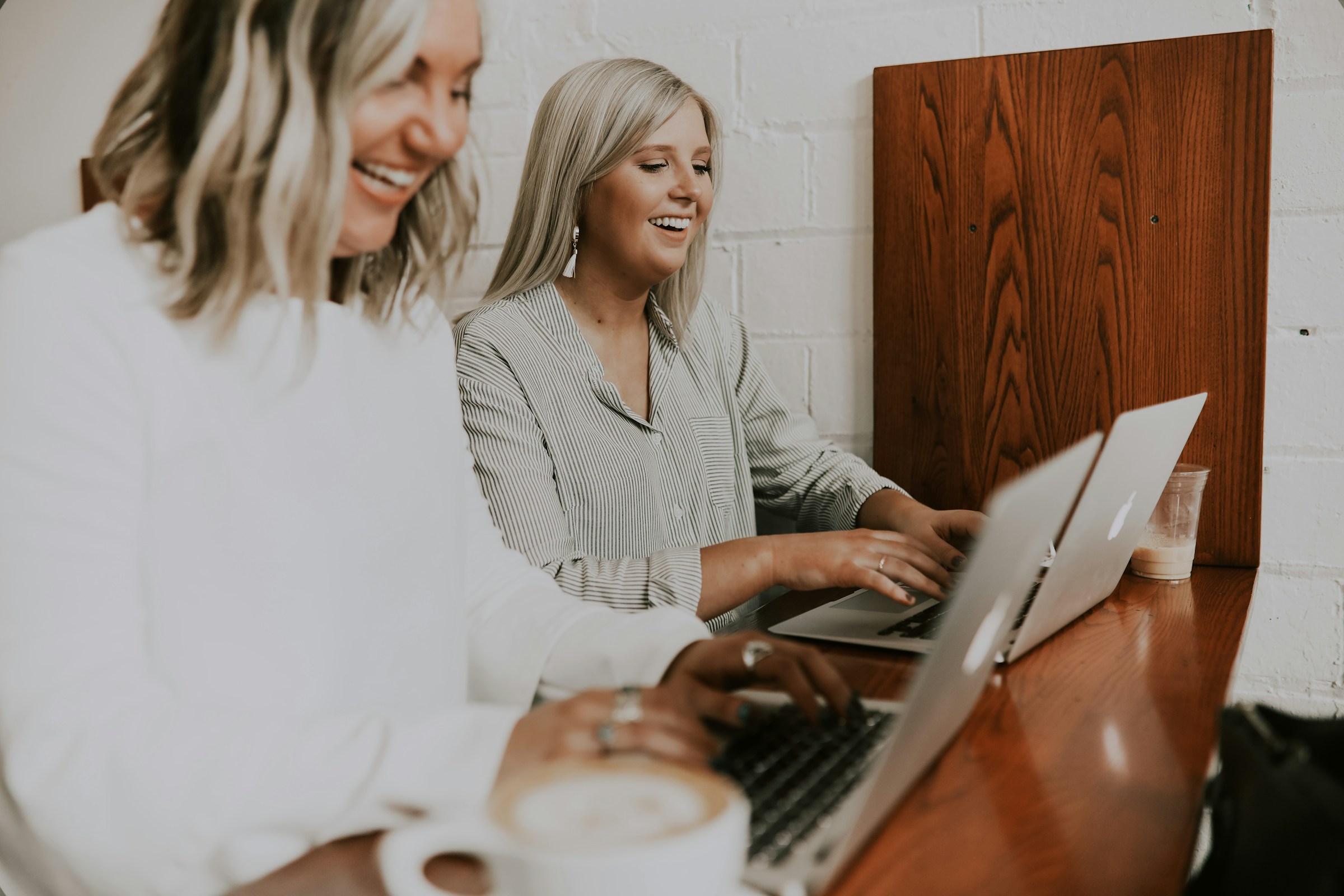 Zwei Frauen lachen, während sie ihre Laptops in einer Büroumgebung benutzen | Quelle: Unsplash