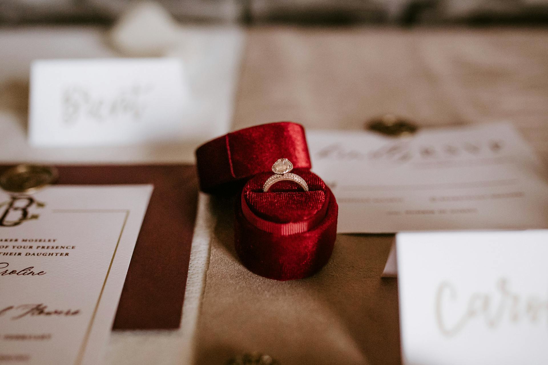 Eine kleine rote Schachtel mit einem Ring auf einem Tisch mit Hochzeitseinladungskarten | Quelle: Pexels