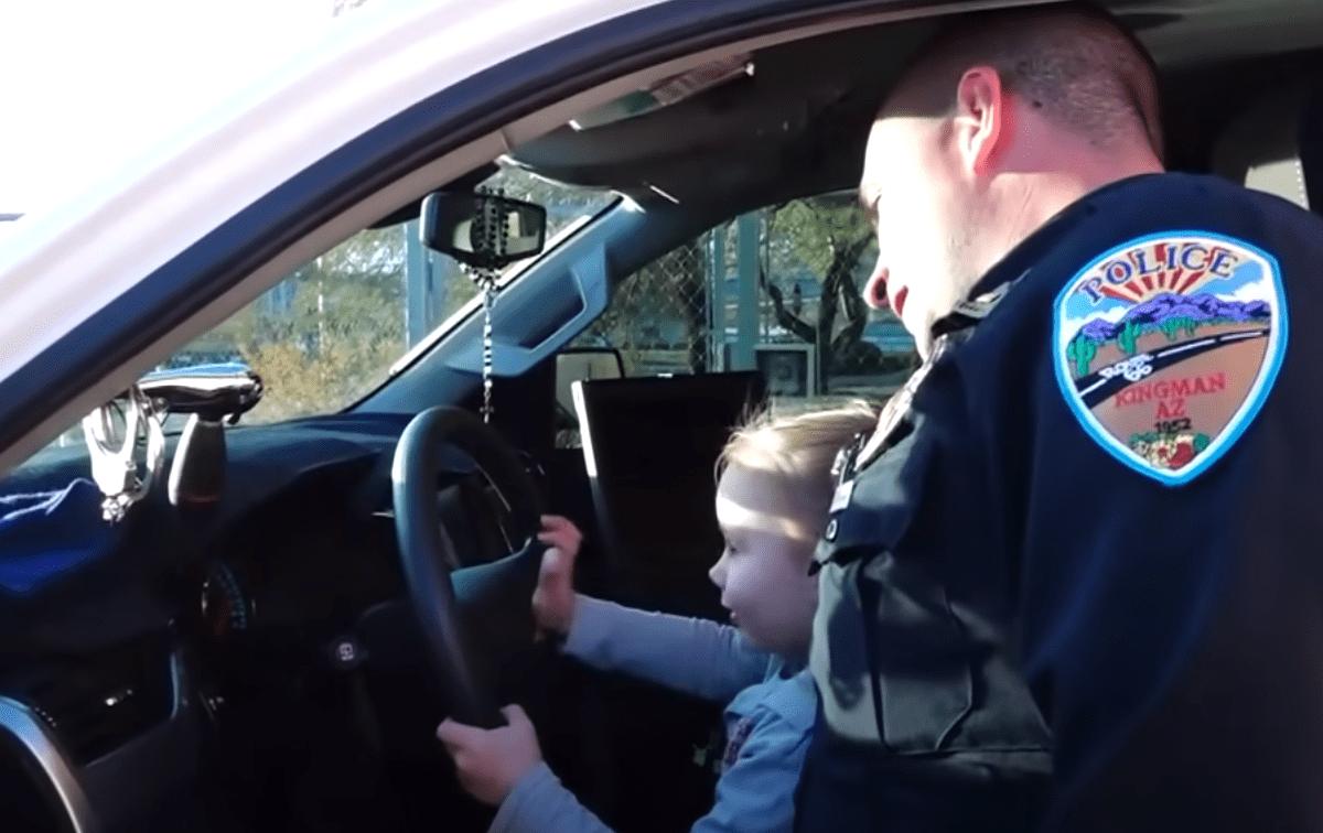 Ein kleines Mädchen sitzt auf dem Schoß ihres Adoptivvaters in einem Polizeifahrzeug | Quelle: Youtube/Inside Edition
