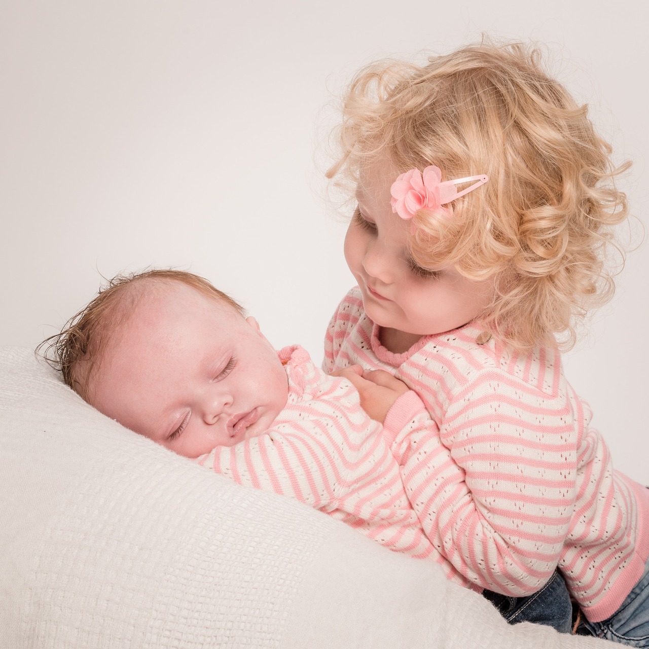 Ein kleines Mädchen, das auf seine schlafende kleine Schwester herabblickt | Quelle: Pixabay