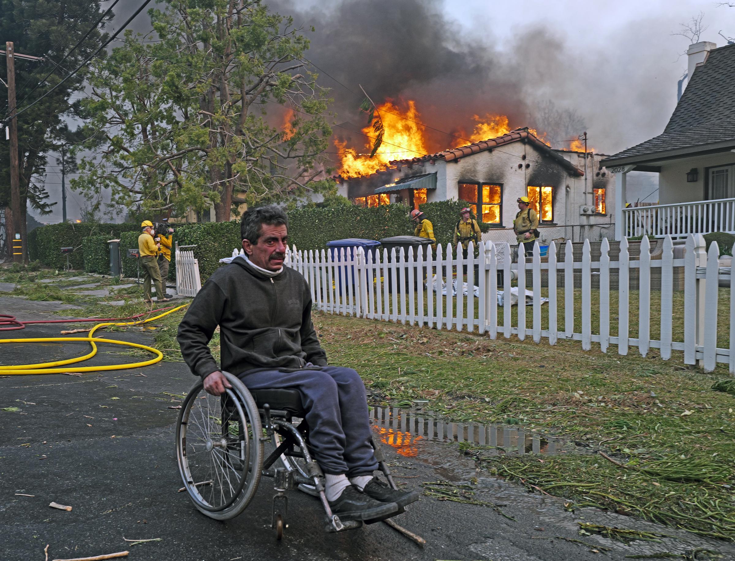 Ein Mann im Rollstuhl fährt am 08. Januar 2025 in Pasadena, Kalifornien, an einem brennenden Haus vorbei, das vom Eaton-Feuer im Stadtteil Altadena betroffen ist | Quelle: Getty Images