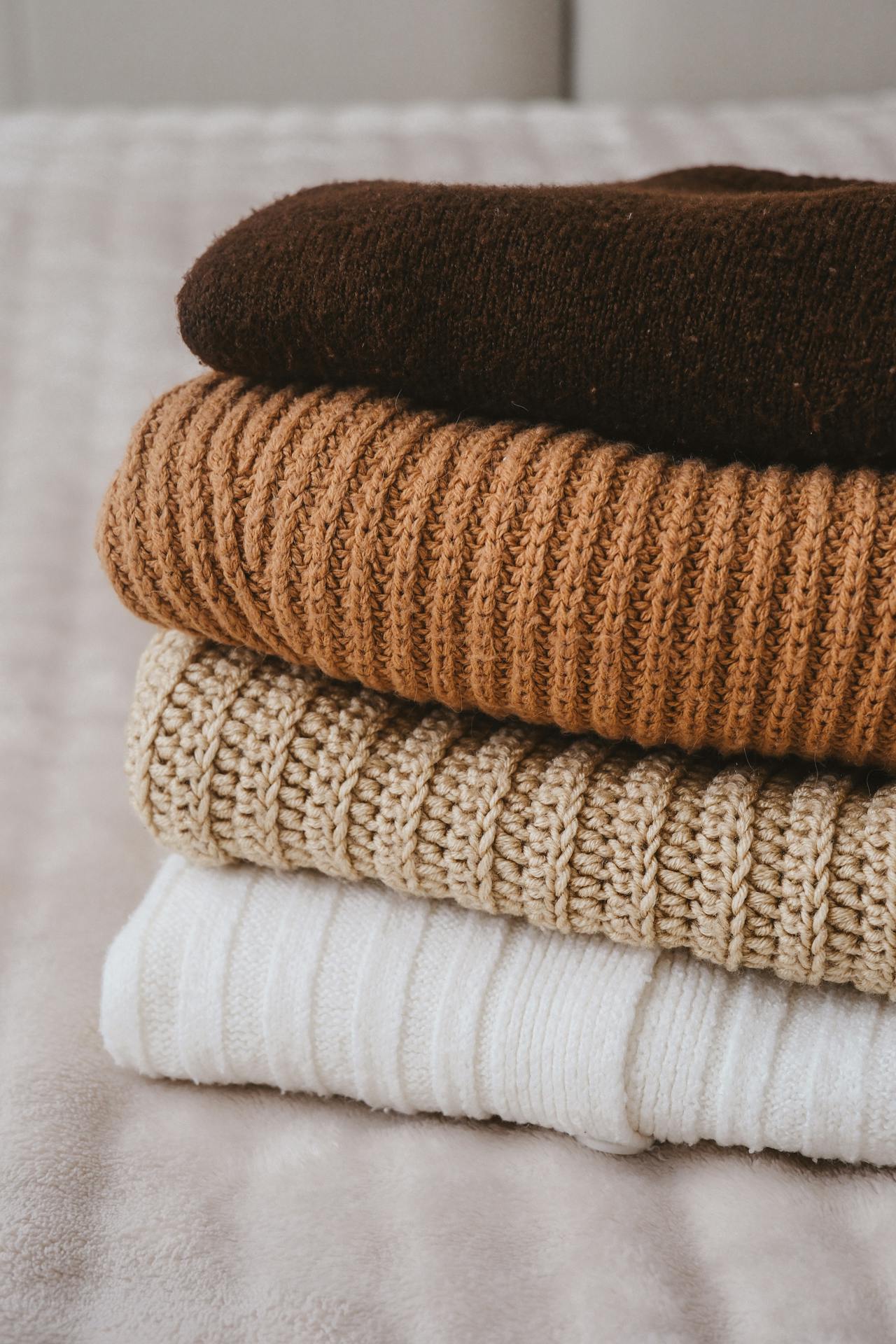 Ein Stapel gefalteter Pullover auf dem Bett | Quelle: Pexels