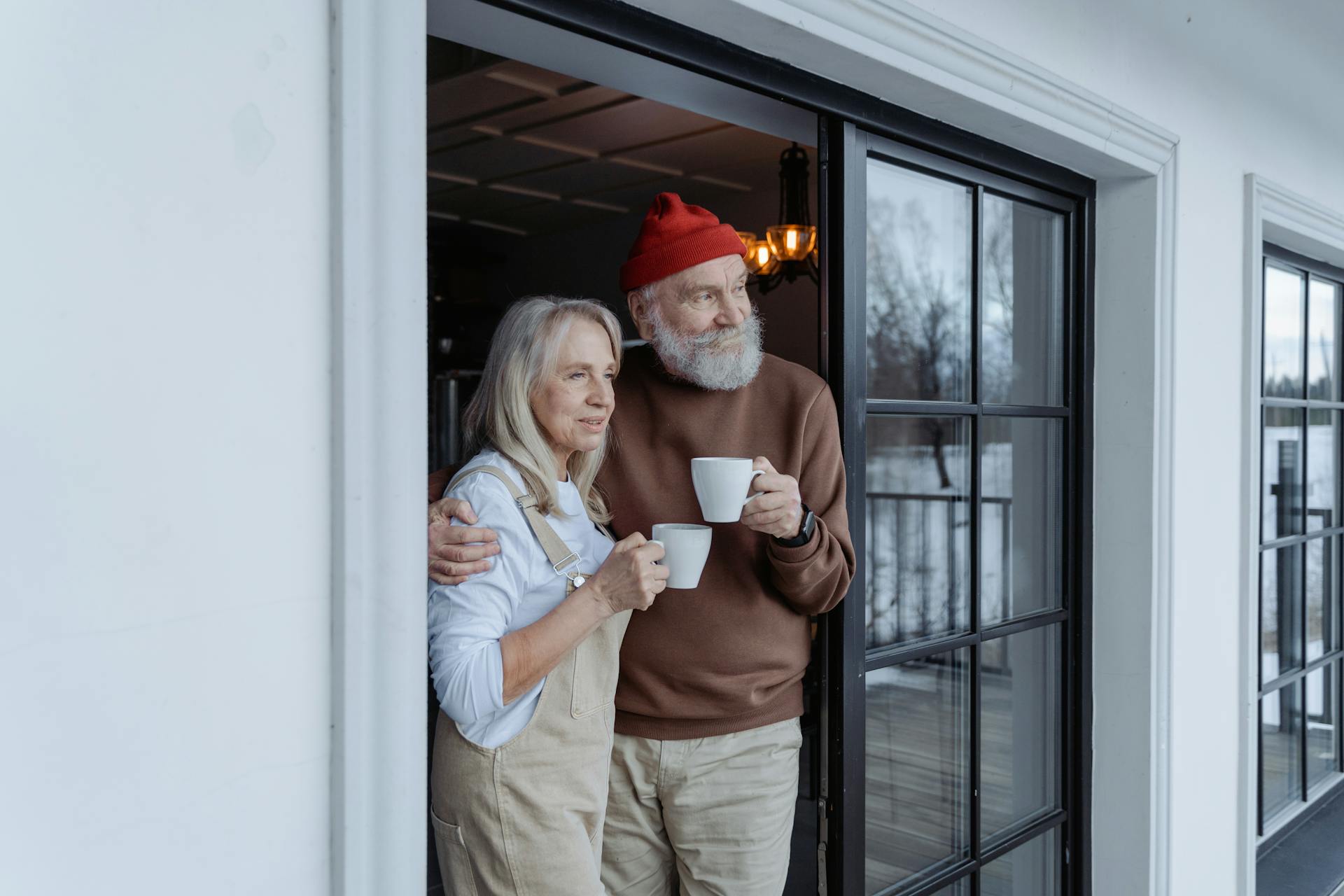 Ein älteres Ehepaar steht vor einer Tür, jeder hält eine Tasse in der Hand | Quelle: Pexels