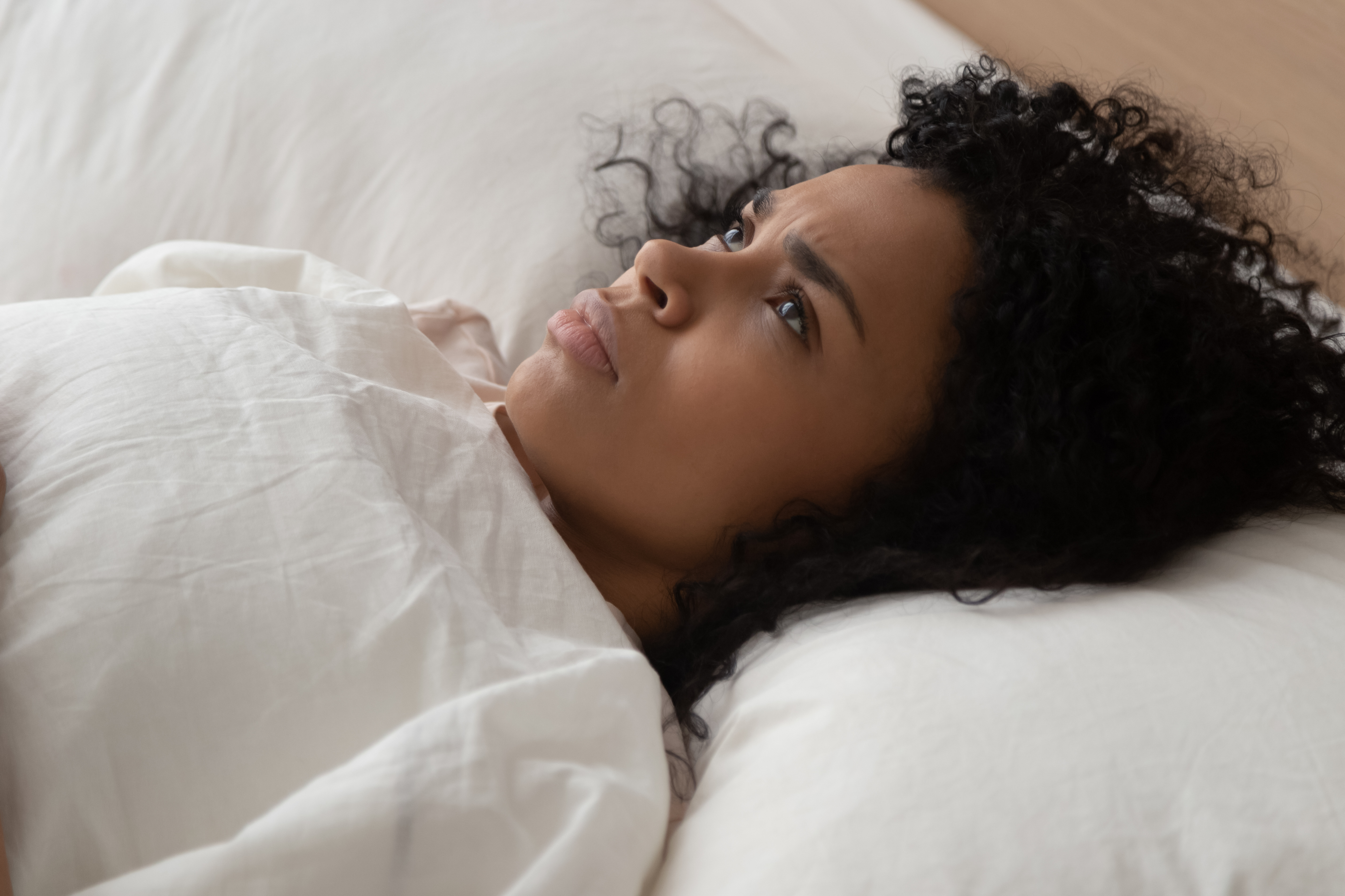 Eine schwarze Frau, die nach oben schaut, während sie Probleme beim Einschlafen hat | Quelle: Shutterstock