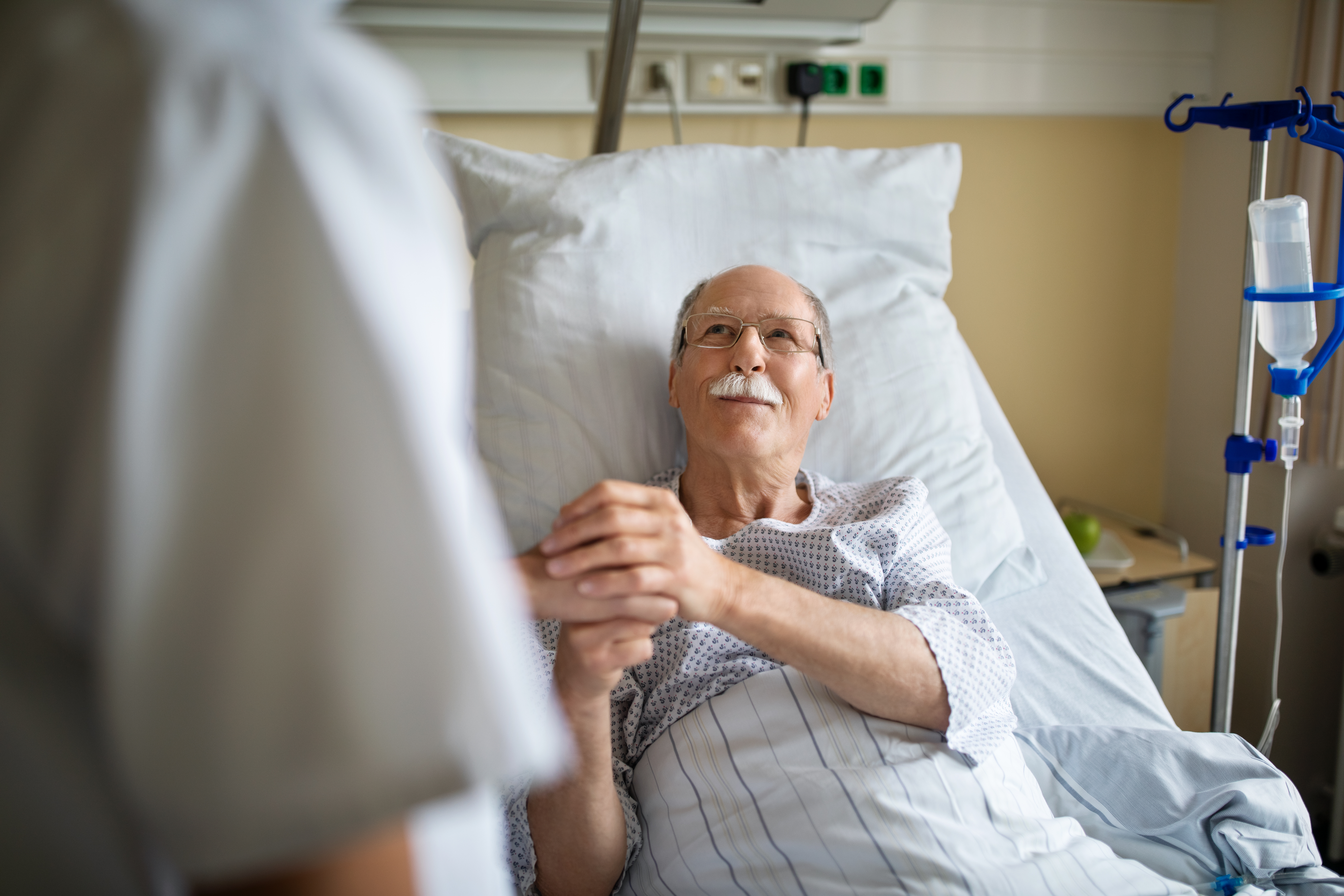 Ein älterer Mann hält die Hand einer Krankenschwester im Krankenhauszimmer | Quelle: Getty Images