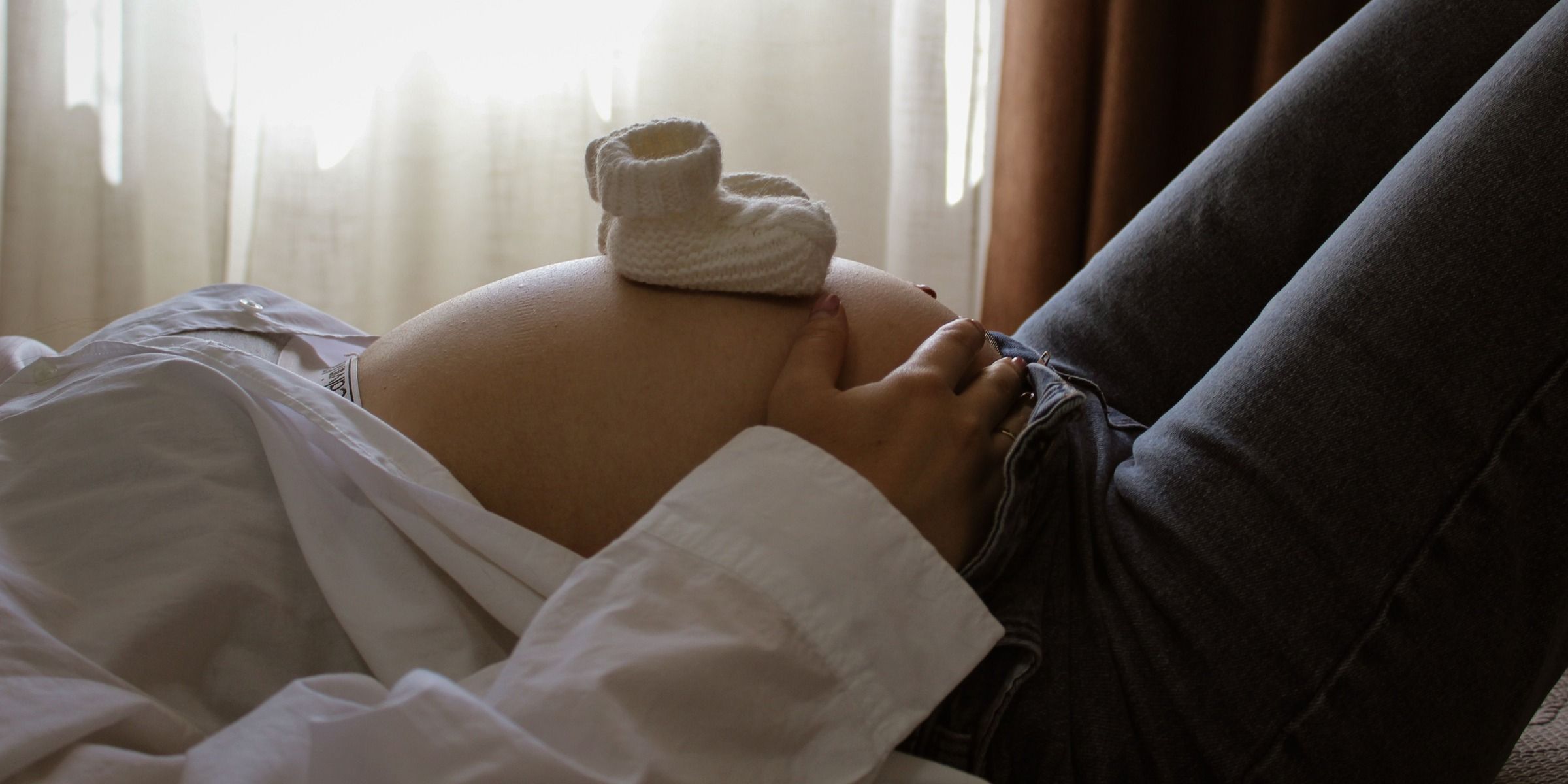 Eine werdende Mutter ruht sich aus, während Baby-Schühchen auf ihrem Bauch liegen | Quelle: Pexels