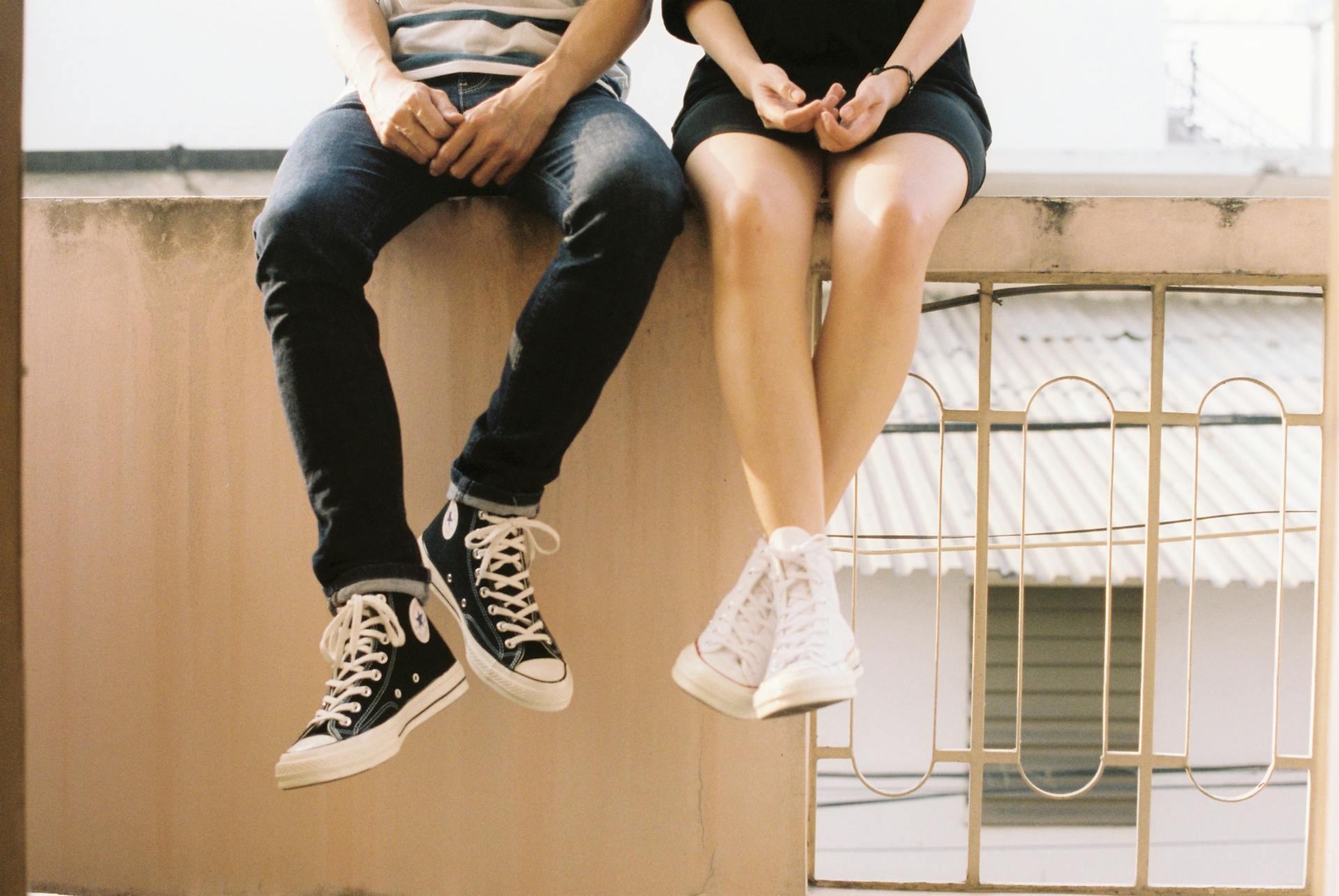 Junges Paar sitzt auf einer Mauer und trägt Converse | Quelle: Pexels