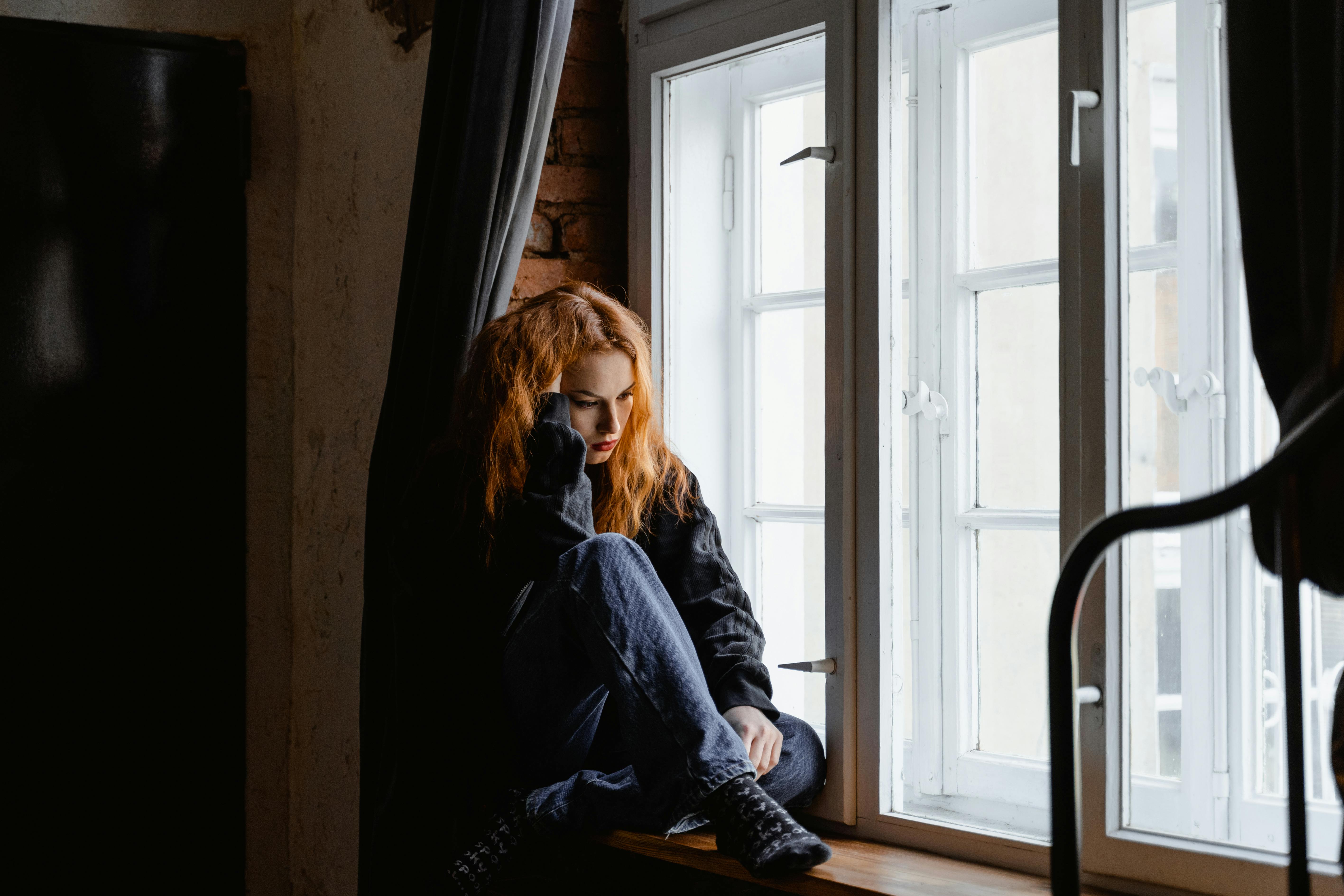 Eine Frau sitzt am Fenster einer Wohnung | Quelle: Pexels