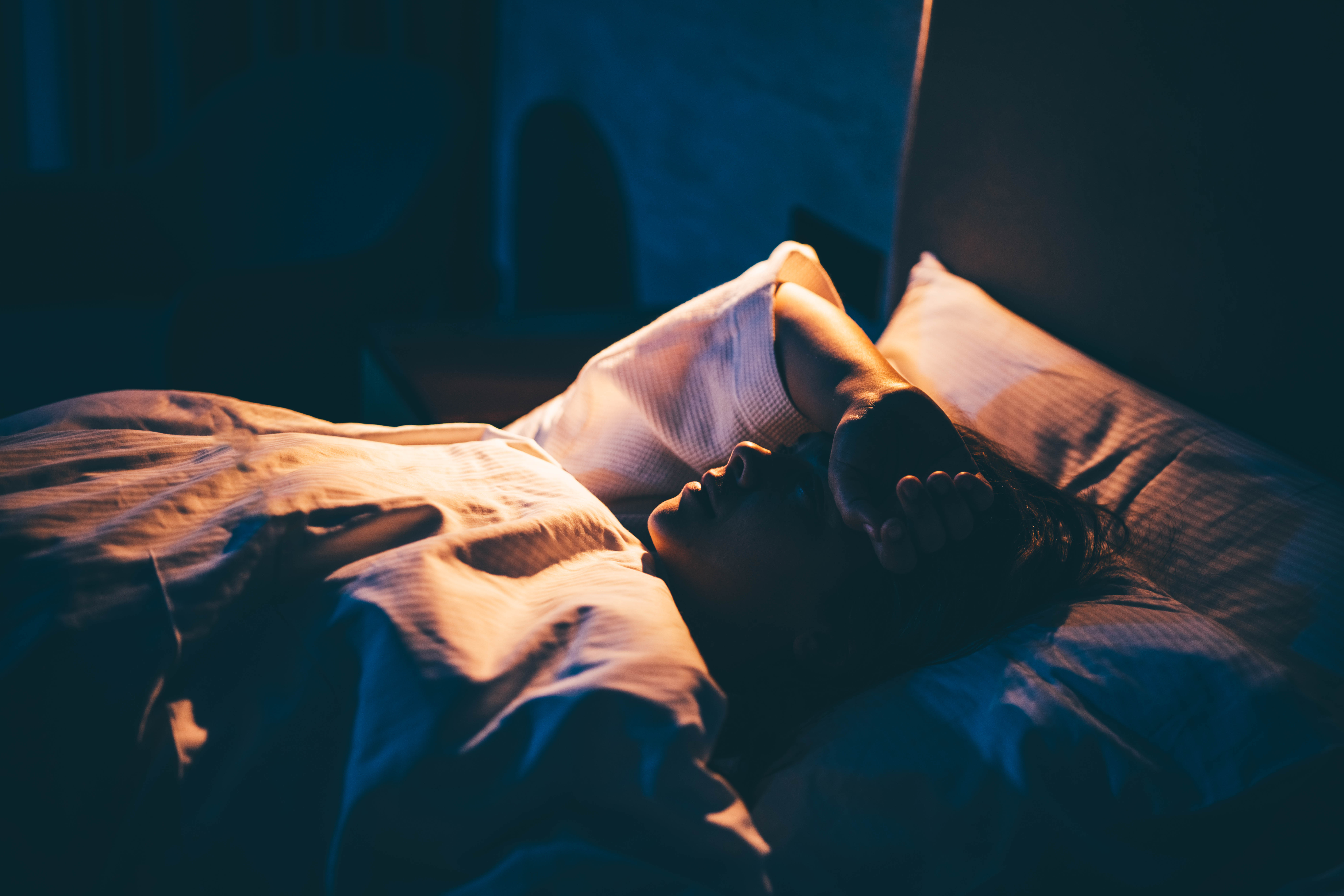 Frau mit Schlaflosigkeit. Junge Frau auf dem Bett liegend mit der Hand auf der Stirn | Quelle: Getty Images