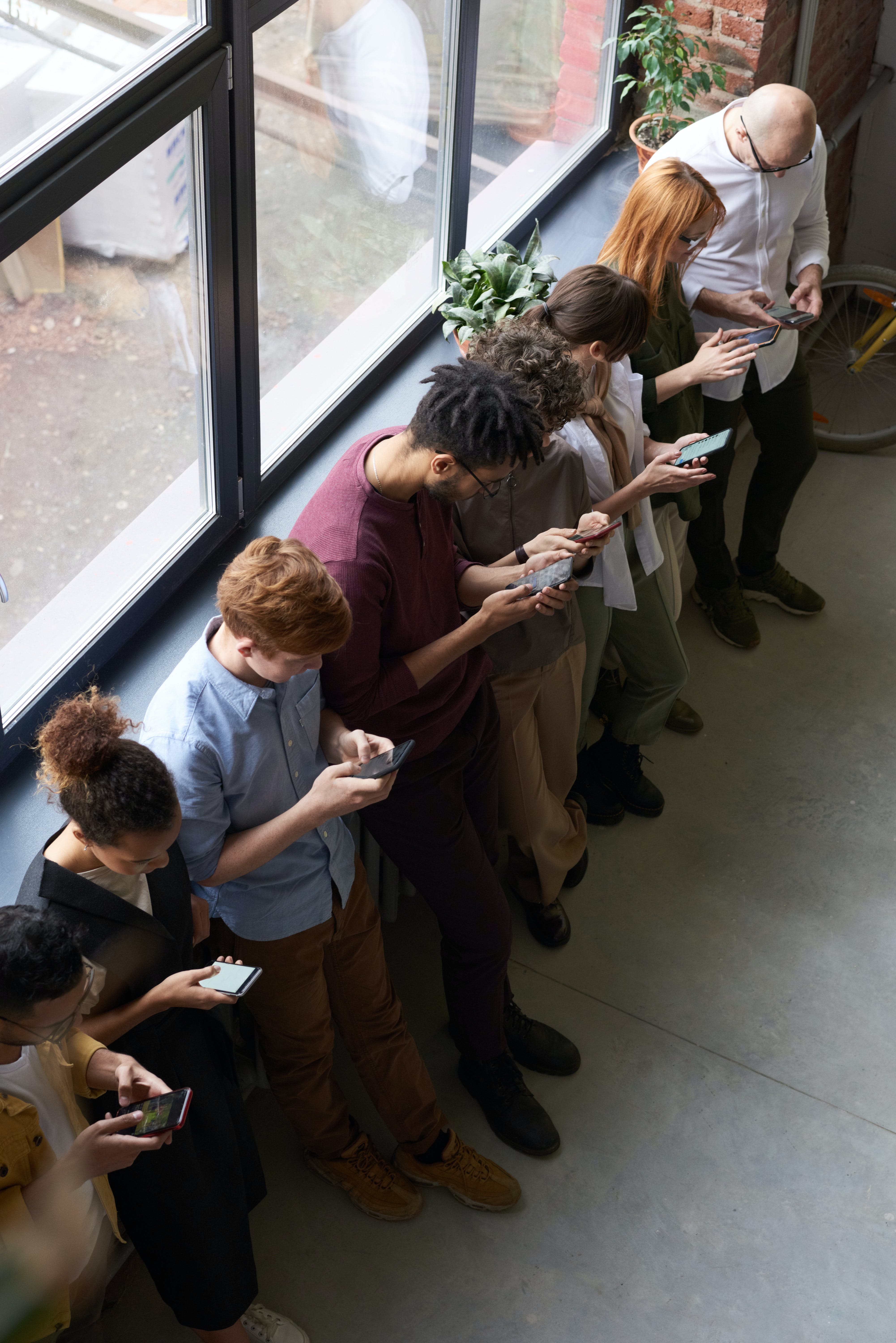 Menschen stehen in einer Warteschlange und bedienen ihre Smartphones. | Quelle: Pexels