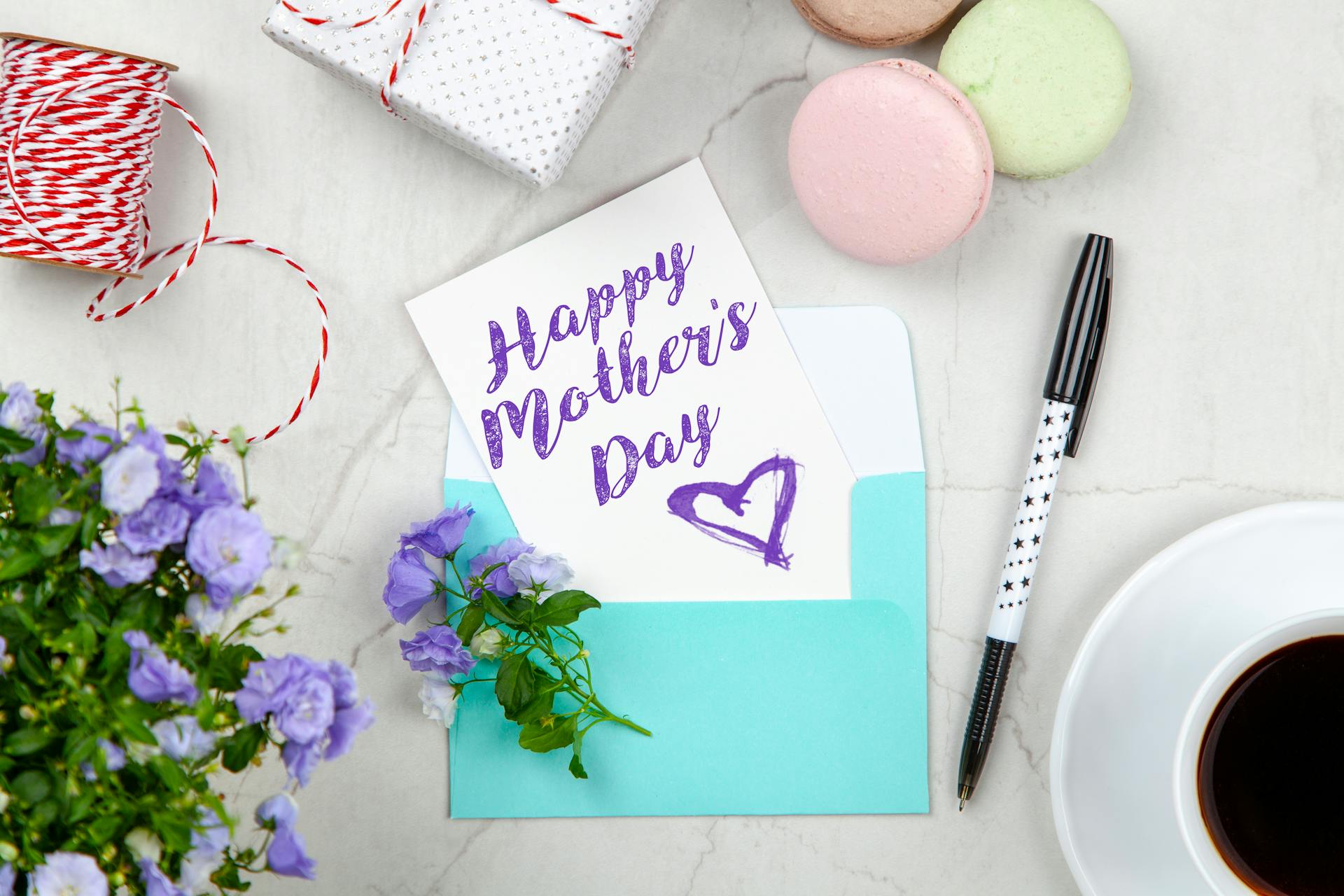 Eine Muttertagskarte neben einem Stift, Makronen, Blumen und einer Schachtel neben einer Kaffeetasse mit Untertasse | Quelle: Pexels