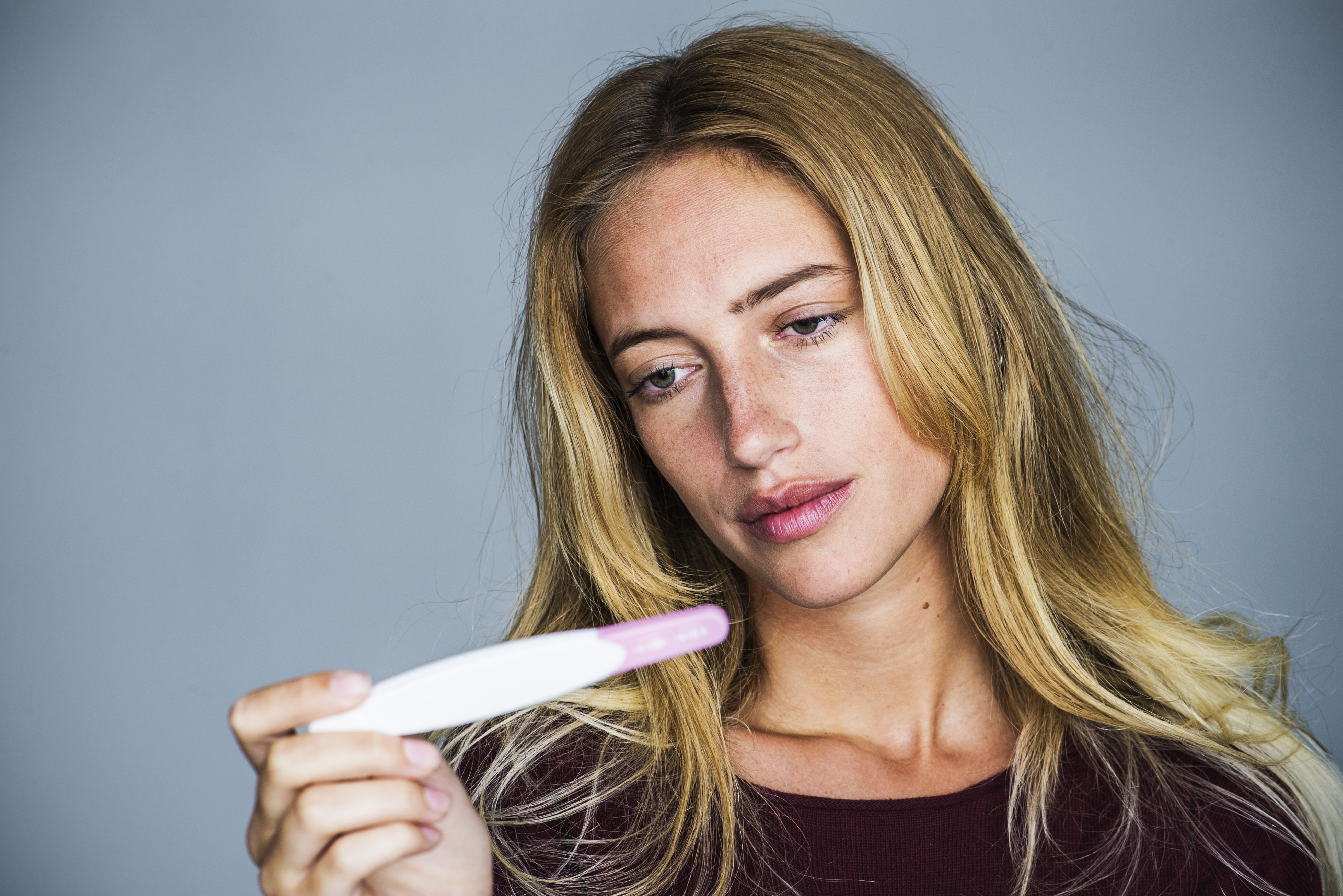 Junge Frau schaut mit enttäuschtem Gesichtsausdruck auf einen Schwangerschaftstest | Quelle: Getty Images