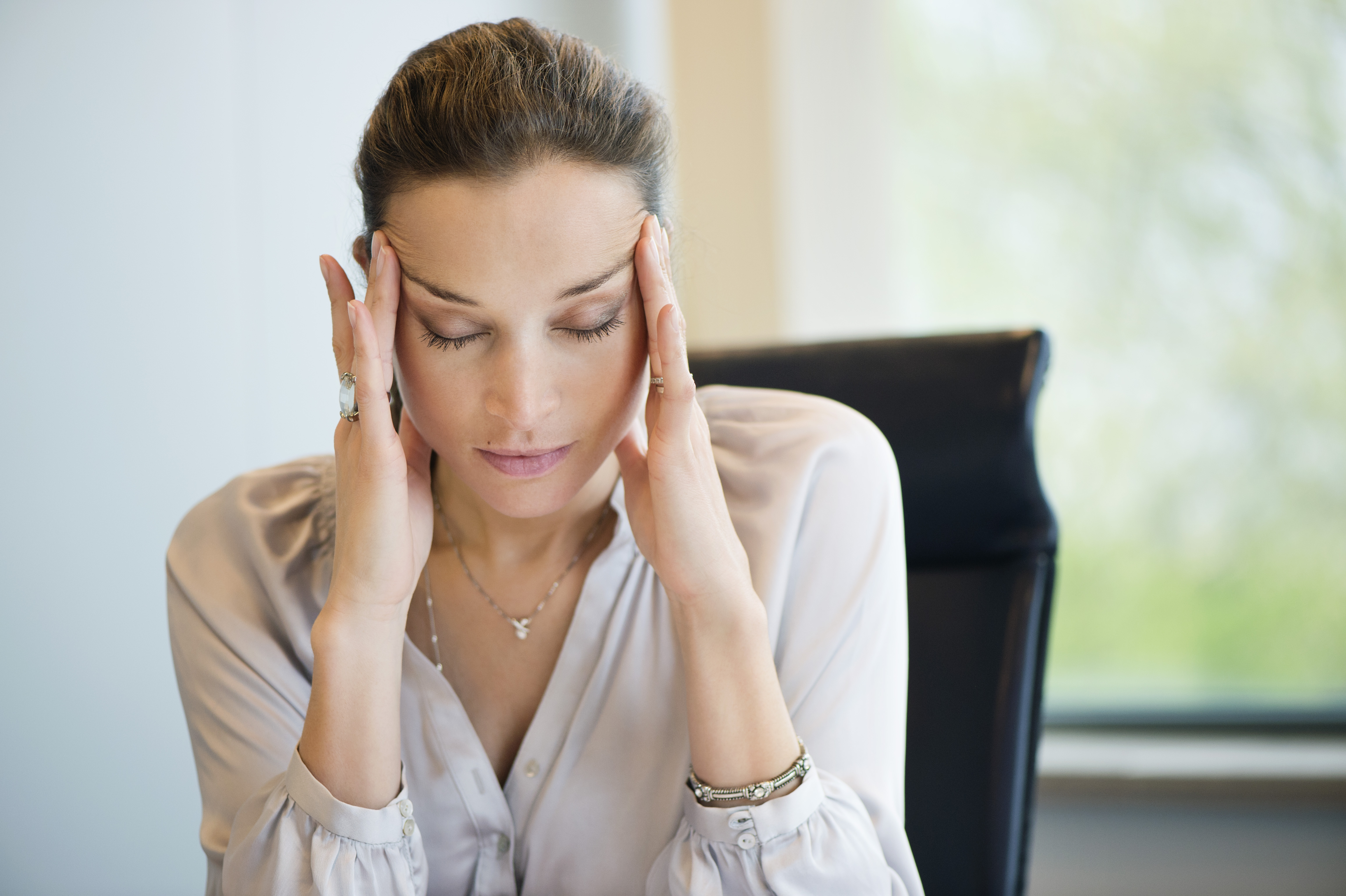 Frau mit Kopfschmerzen bei der Arbeit in einem Büro | Quelle: Getty Images