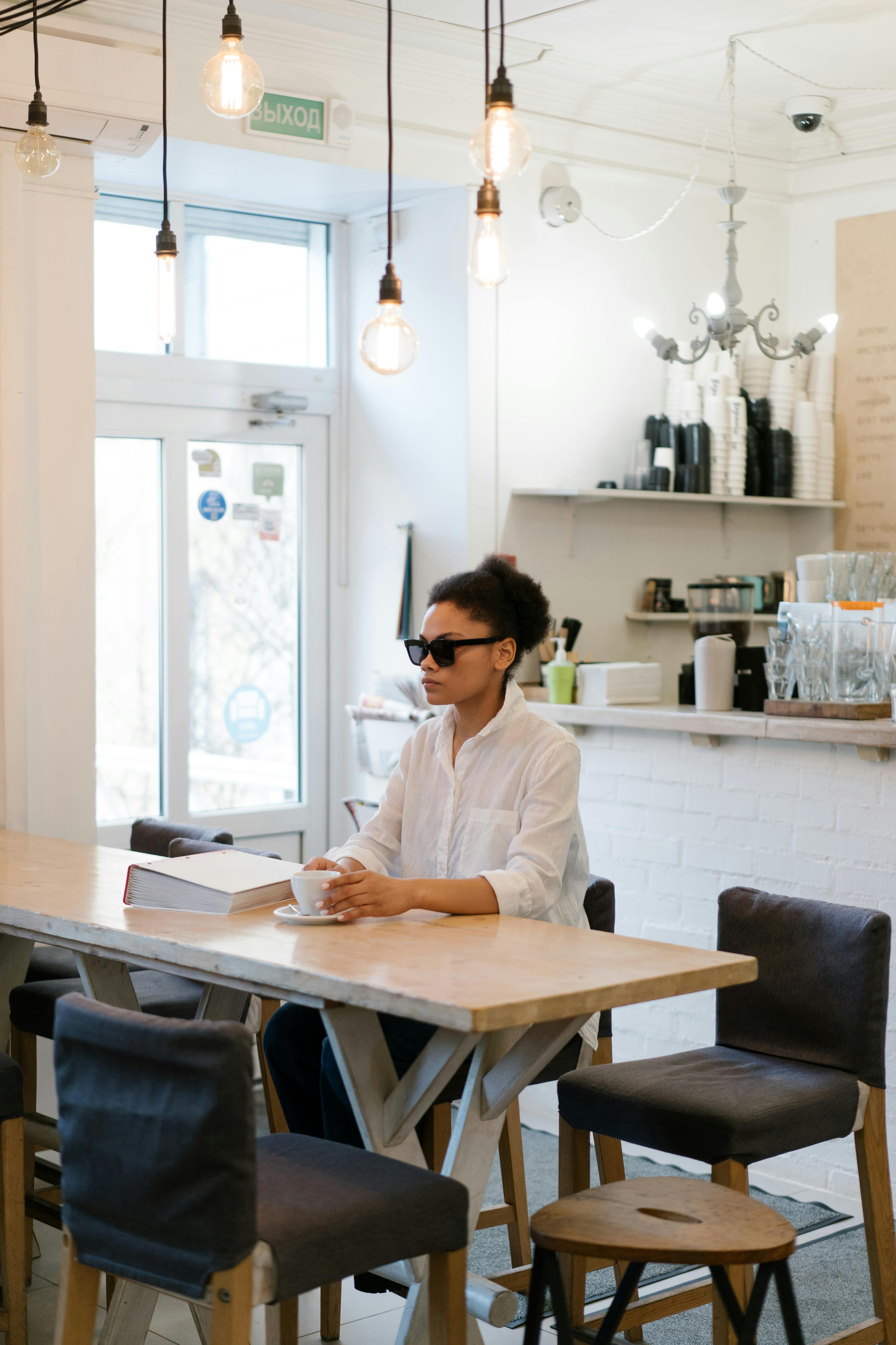 Eine Frau mit Sonnenbrille sitzt an einem Tisch in einem Café | Quelle: Pexels