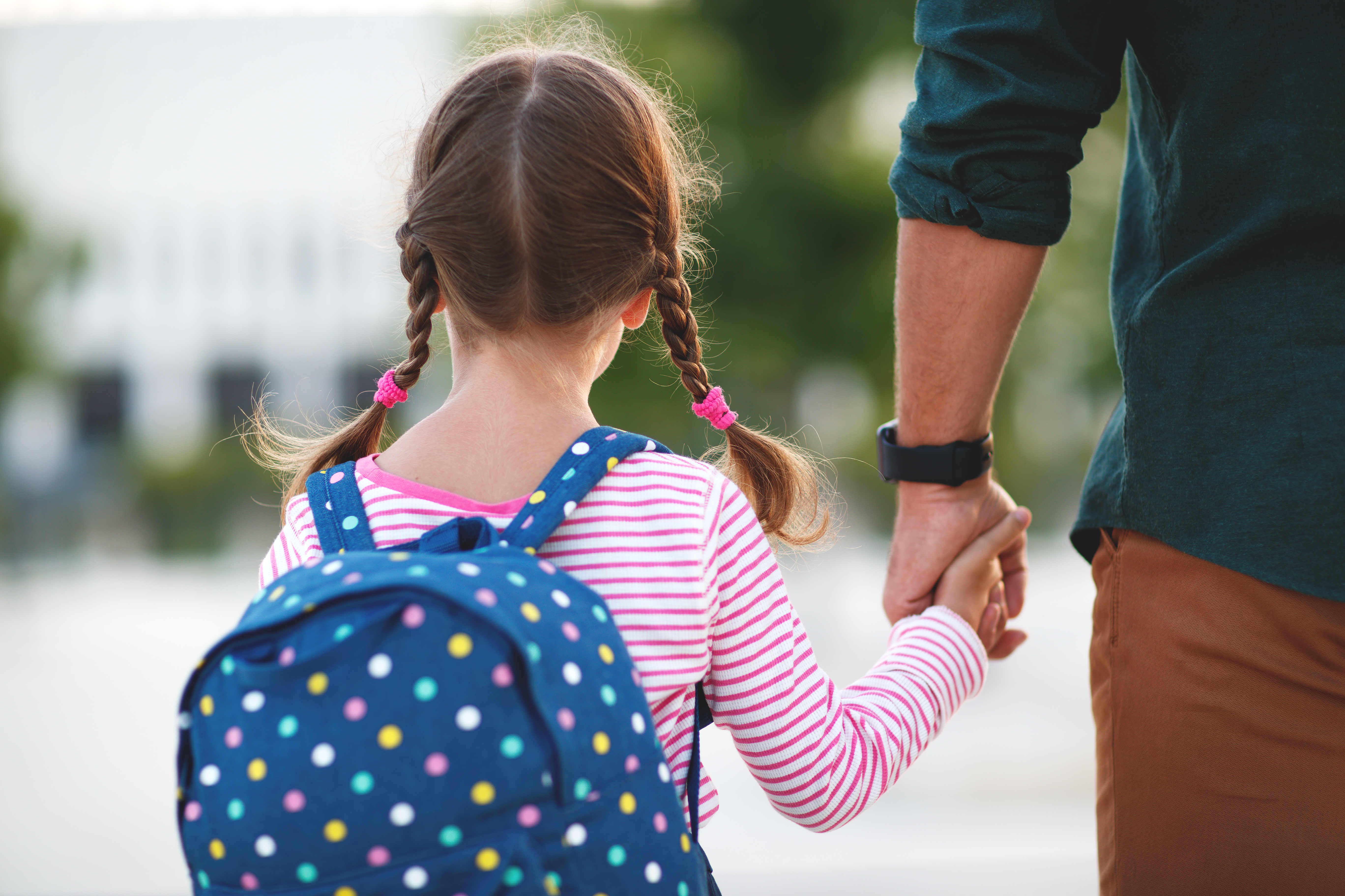 Ein kleines Mädchen hält die Hand ihres Vaters auf dem Weg zur Schule | Quelle: Shutterstock