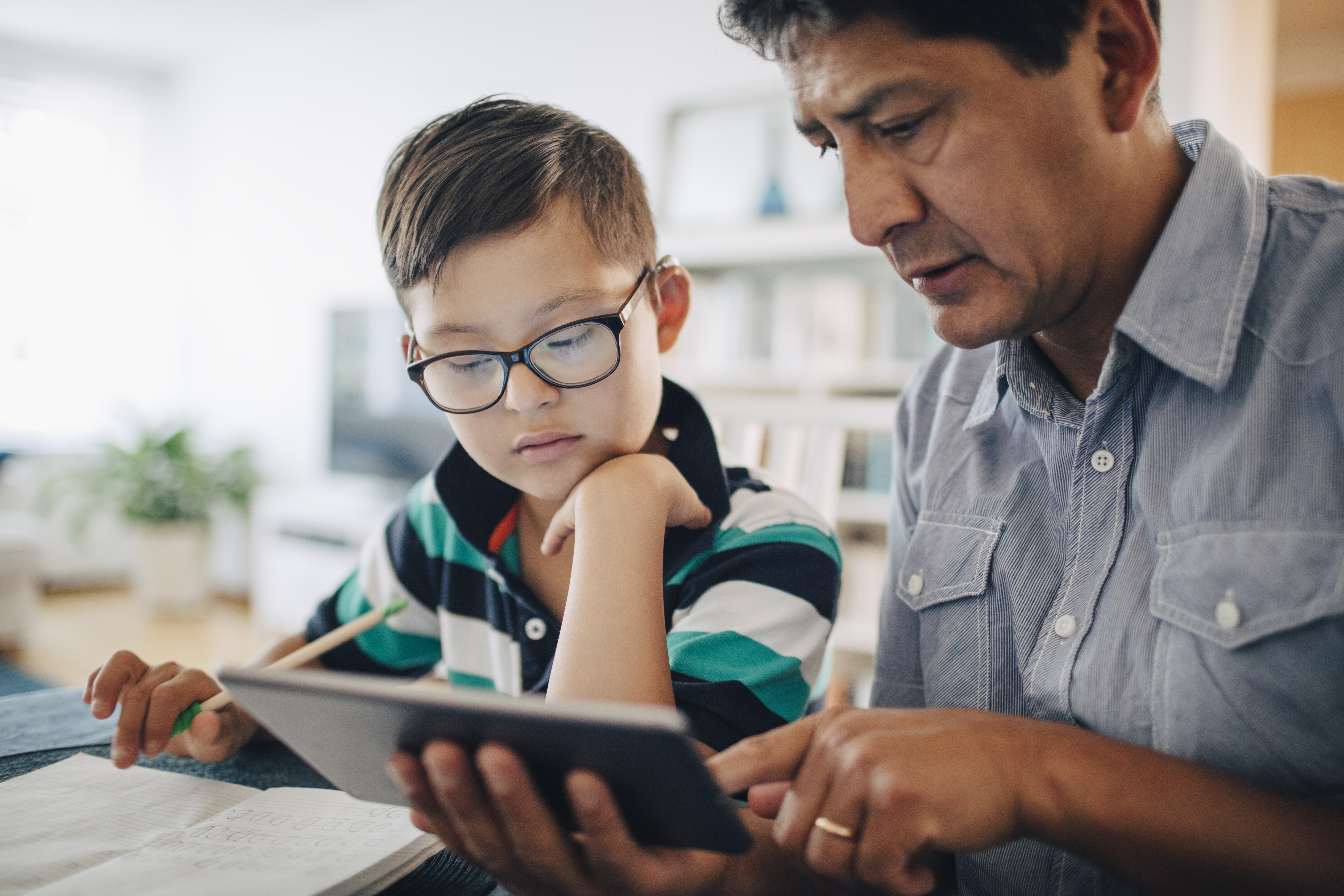 Vater zeigt seinem Sohn ein digitales Tablet, während er am Tisch lernt | Quelle: Getty Images