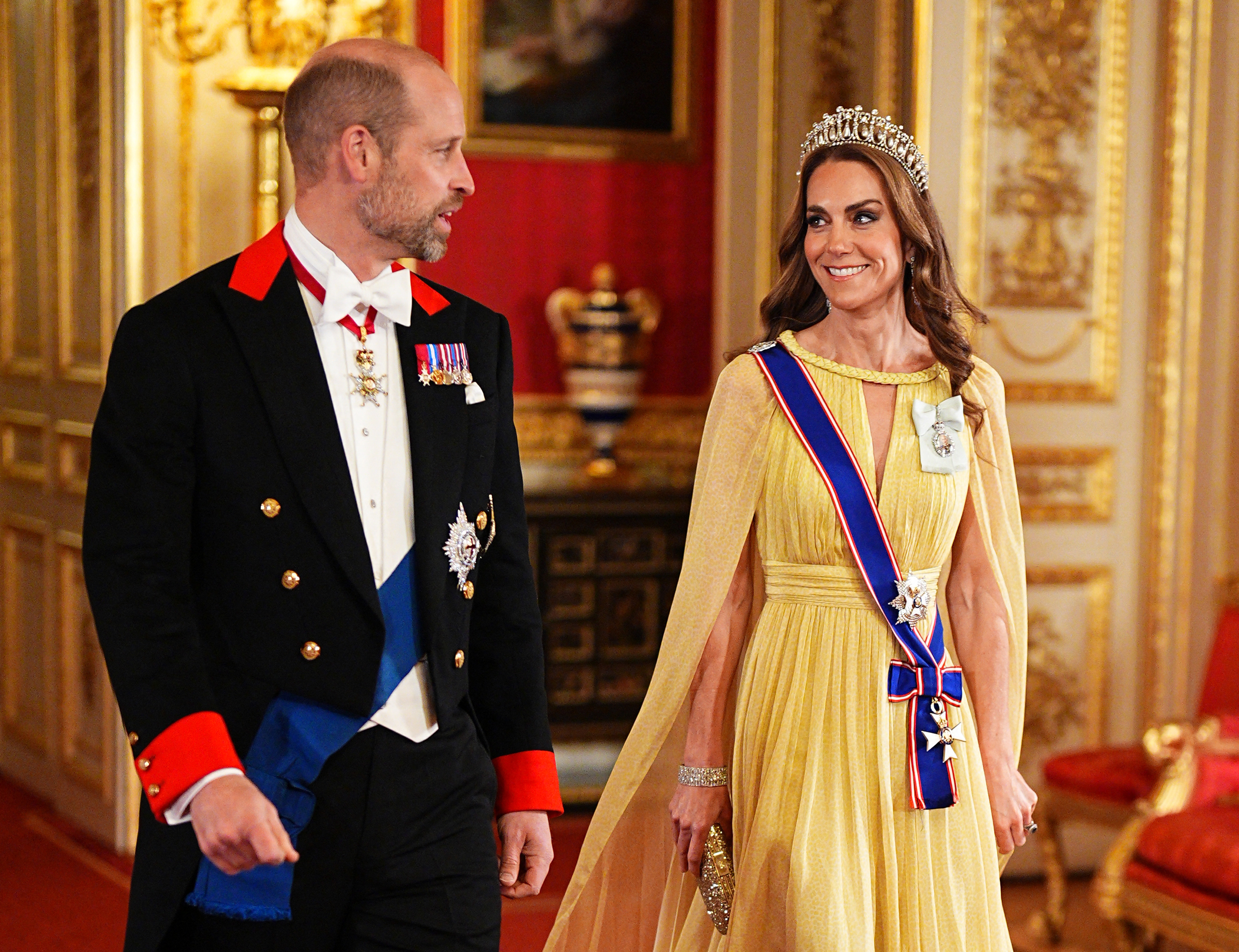Catherine, Prinzessin von Wales, tauscht ein fröhliches Lächeln mit Prinz William aus, während sie am 20. Oktober 2026 durch die prächtigen Empfangssäle von Windsor Castle schreiten. Gekrönt mit Königin Marys „Lover’s Knot“-Tiara sieht Catherine in einem fließenden, butterblumengelben Cape-Kleid von Elie Saab, verziert mit der Schärpe des Royal Victorian Order und dem Royal Family Order von König Charles III., einfach umwerfend aus, während William neben ihr in einem formellen Windsor-Frack mit der Schärpe des Hosenbandordens schreitet. | Quelle: Getty Images