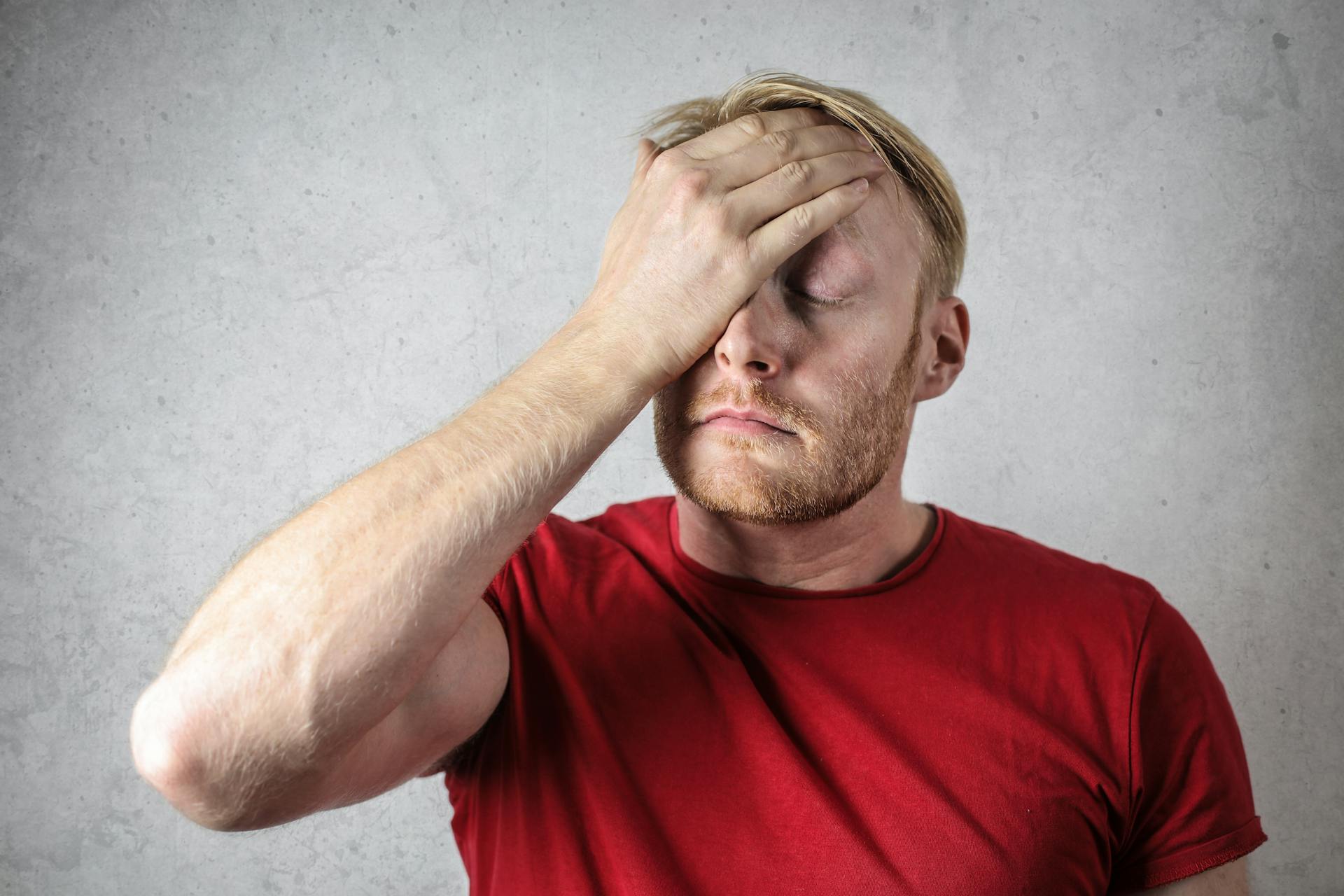 Ein verärgerter Mann im roten T-Shirt, der sein Gesicht verdeckt | Quelle: Pexels