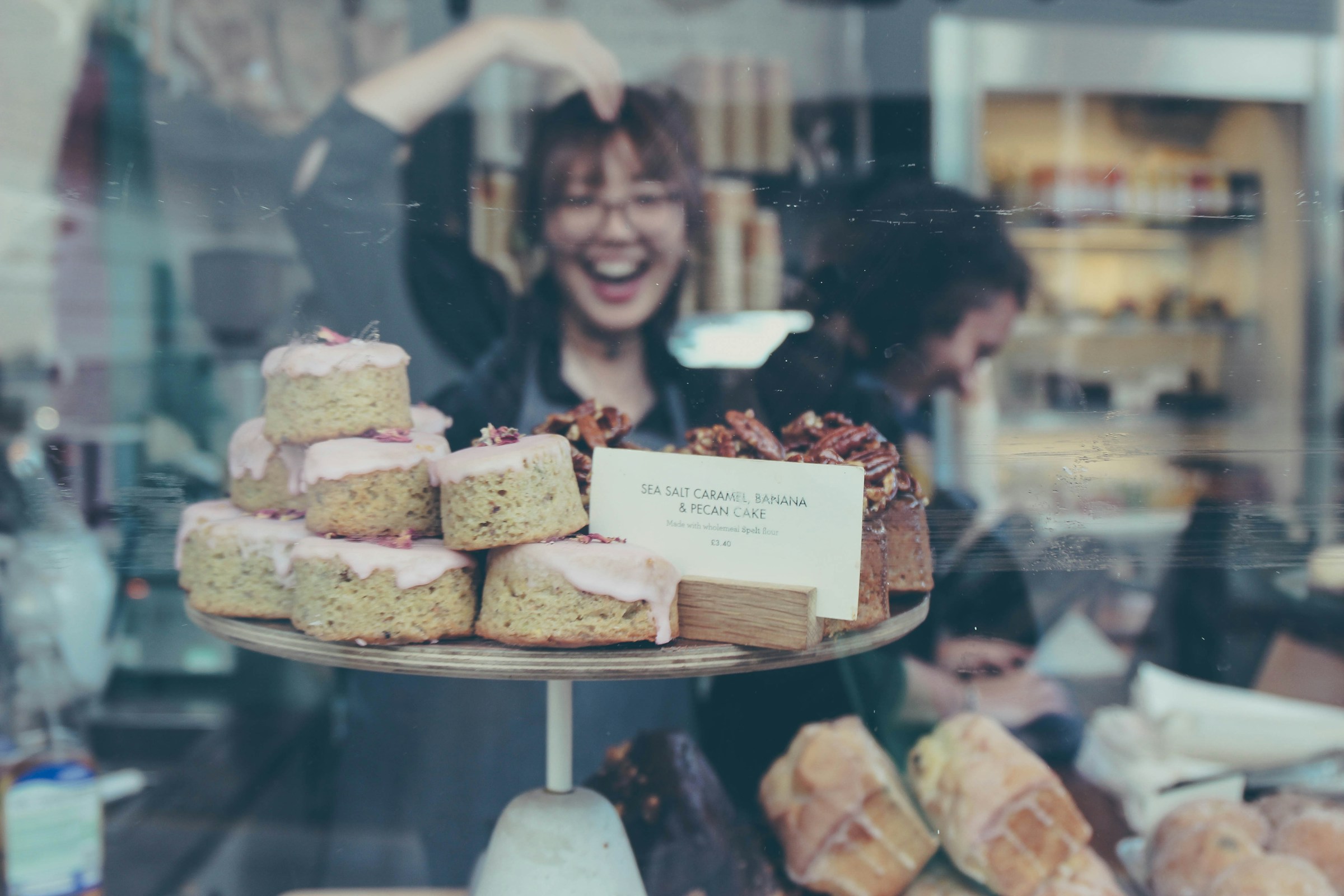 Das Spiegelbild einer lächelnden jungen Frau im Glas einer Bäckereiauslage | Quelle: Unsplash