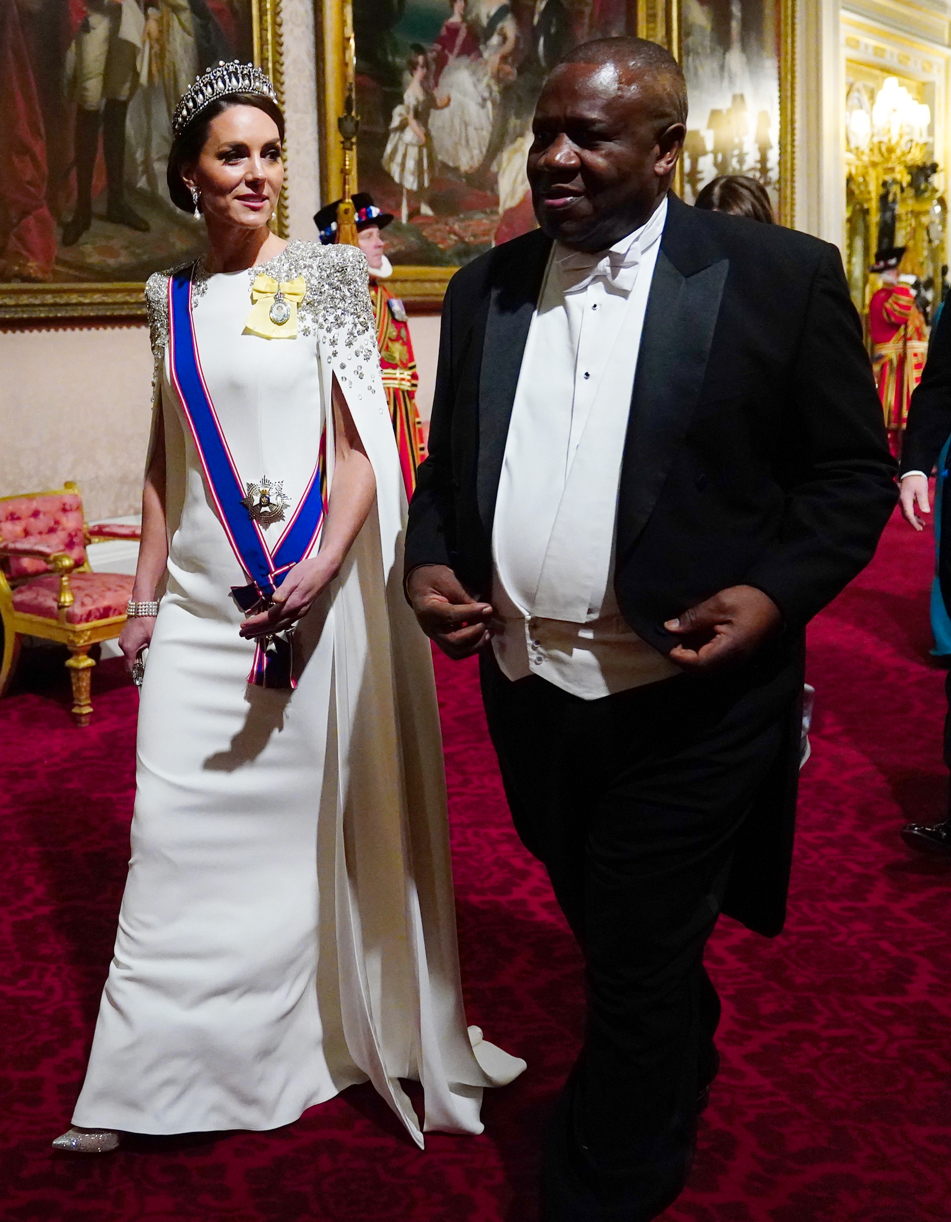 Catherine, Prinzessin von Wales, trifft am 22. November 2022 im Buckingham Palace zum Staatsbankett zu Ehren des südafrikanischen Präsidenten Cyril Ramaphosa ein – ihr erster Bankettauftritt in dieser Rolle. Sie trägt ein elfenbeinfarbenes Cape-Kleid von Jenny Packham mit kristallverzierten Schultern, dazu die „Lover’s Knot“-Tiara von Königin Mary, Prinzessin Dianas Perlenohrringe und königliche Auszeichnungen. | Quelle: Getty Images