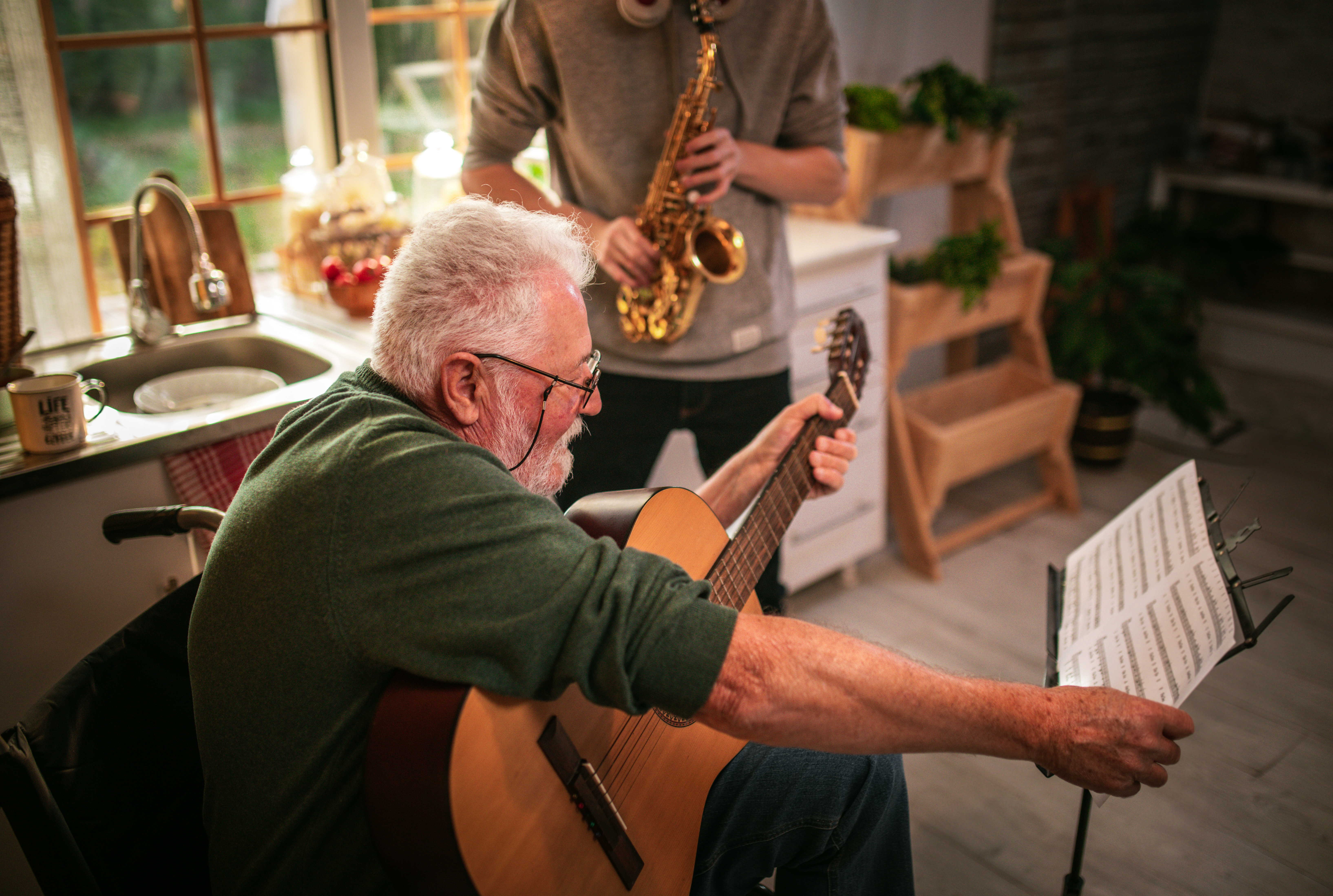 Ein glücklicher älterer Mann und sein Enkel haben Spaß, während sie zu Hause Saxophon und Gitarre spielen. | Quelle: Getty Images