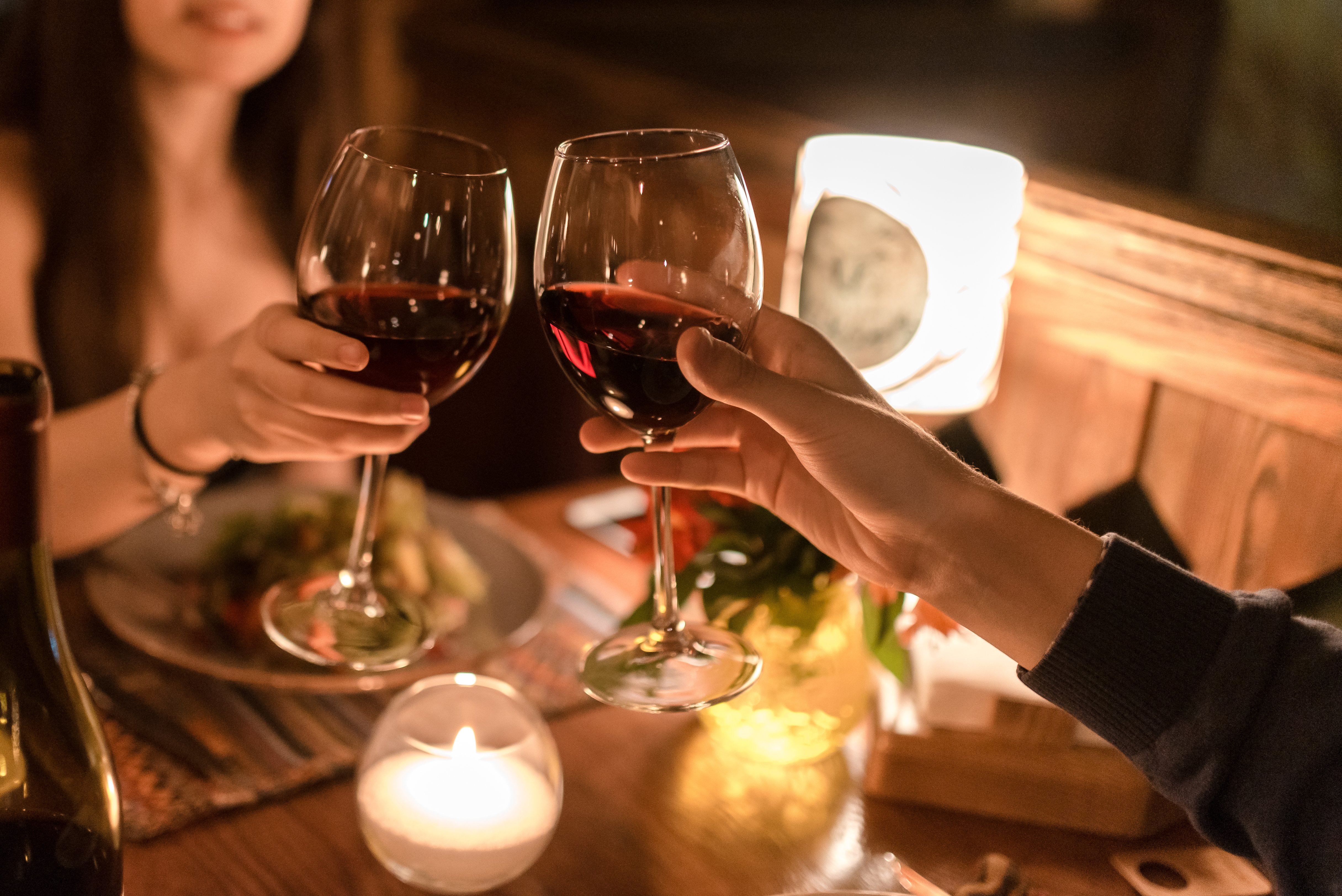 Hand des Mannes und der Frau, die in einem dunklen Restaurant an einem Tisch sitzen und Gläser mit Rotwein halten | Quelle: Shutterstock