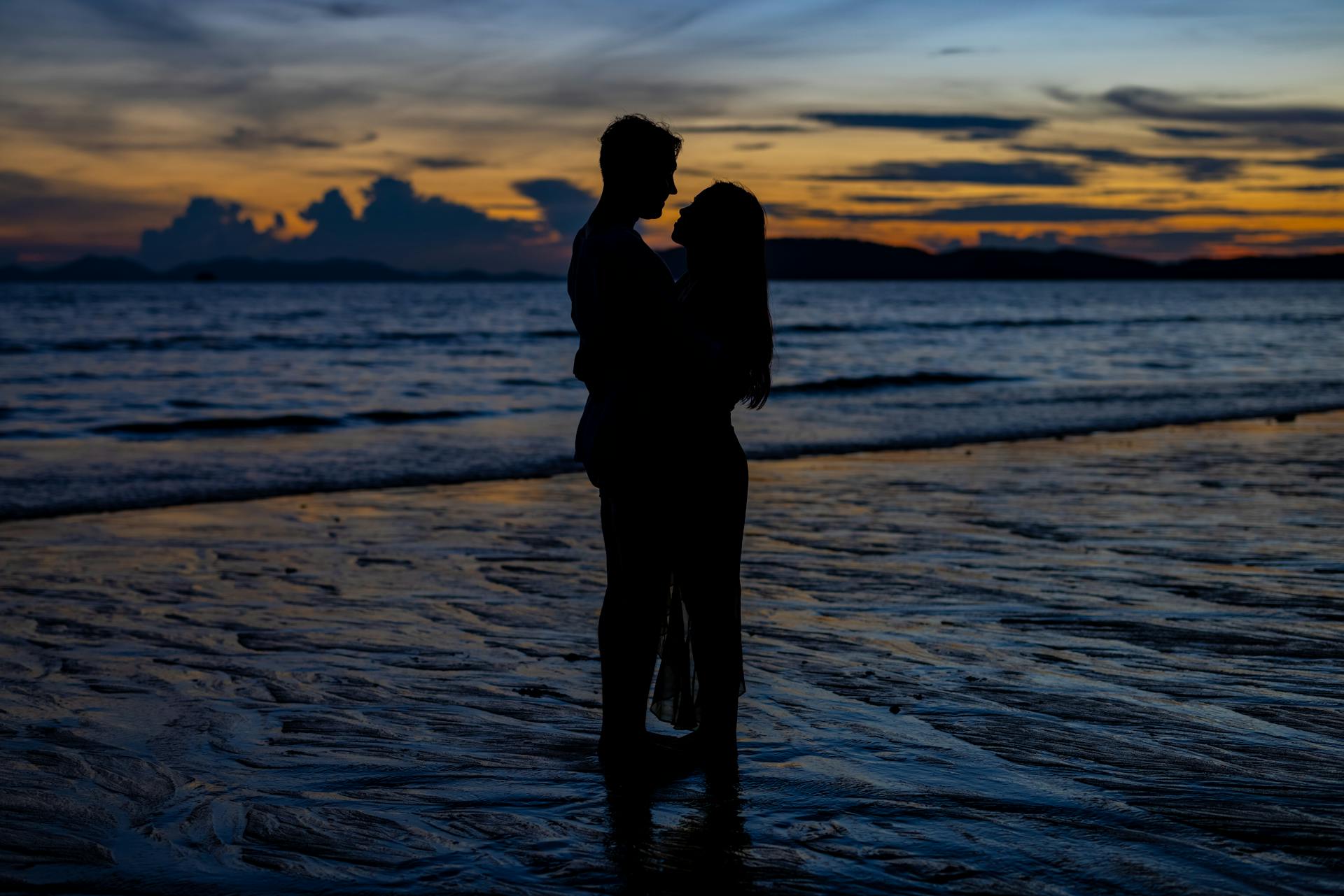 A silhueta de um casal apaixonado abraçado à beira-mar ao pôr do sol | Fonte: Pexels