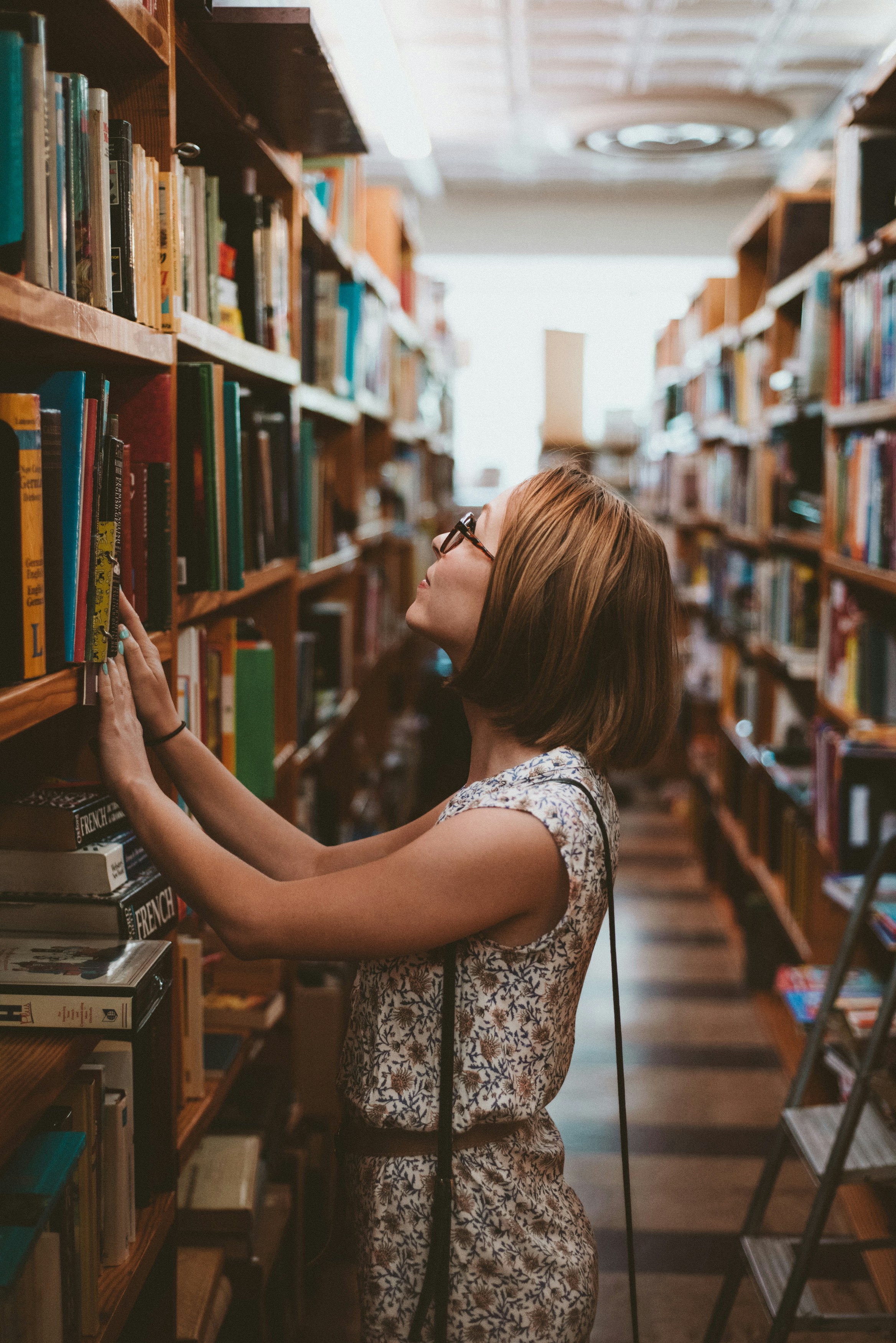 Eine Frau greift nach einem Buch in einer Bibliothek | Quelle: Unsplash