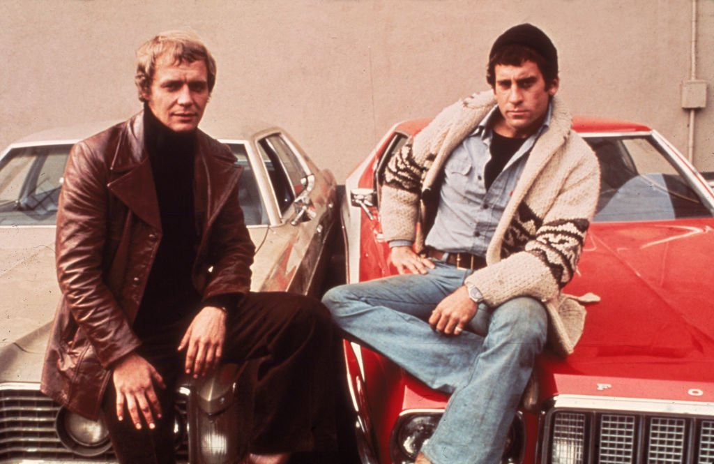 Werbeporträt der amerikanischen Schauspieler David Soul und Paul Michael Glaser, die auf den Motorhauben ihrer Autos sitzen, aus der Fernsehserie "Starsky and Hutch", um 1977 | Quelle: Getty Images
