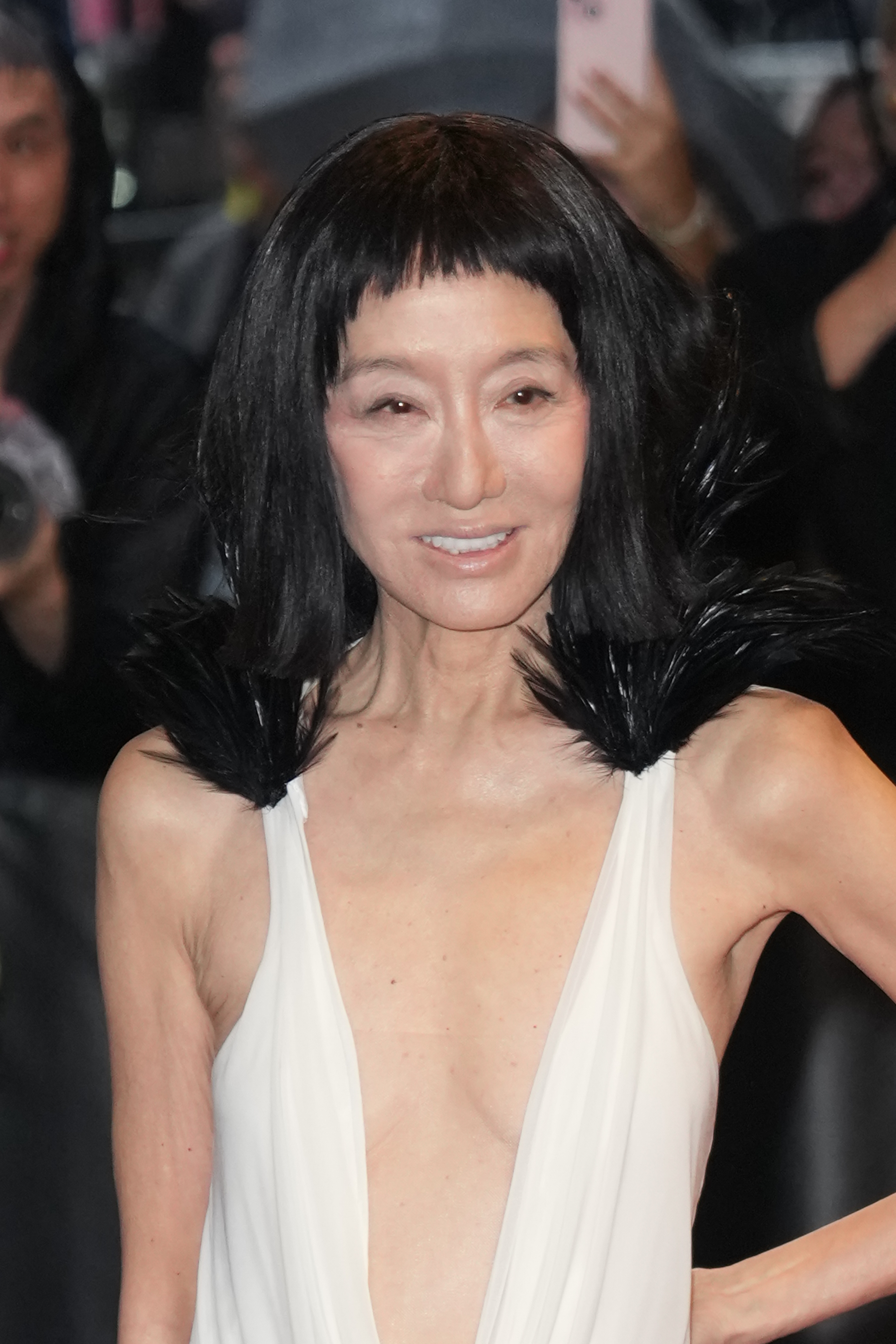 Vera Wang lächelt in einem tief ausgeschnittenen elfenbeinfarbenen Kleid mit dramatischen Federakzenten in die Kameras und zeigt damit eine sanftere Seite ihres kühnen Ensembles für den roten Teppich.