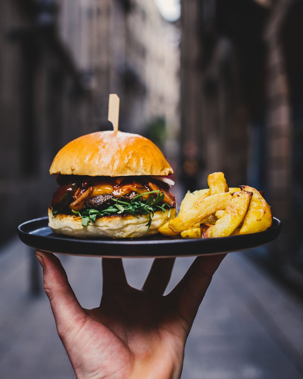 Ein Kellner serviert einen Teller mit einem Burger und Pommes Frites | Quelle: Pixabay