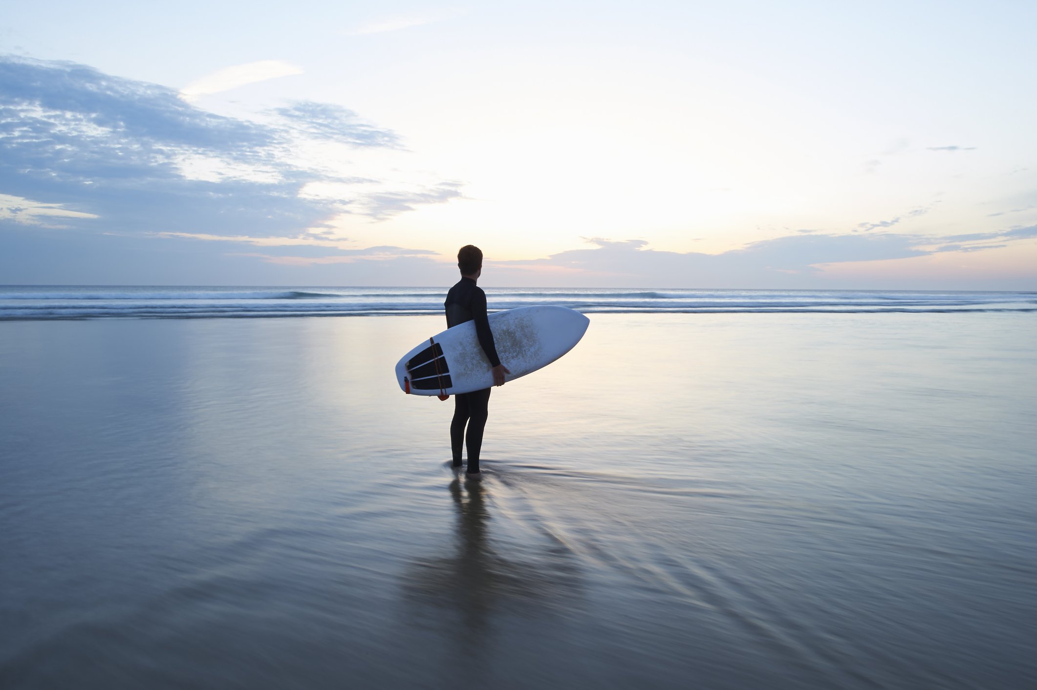 Surfer mit Surfbrett mit Blick auf das Meer in der Abenddämmerung | Quelle: Getty Images