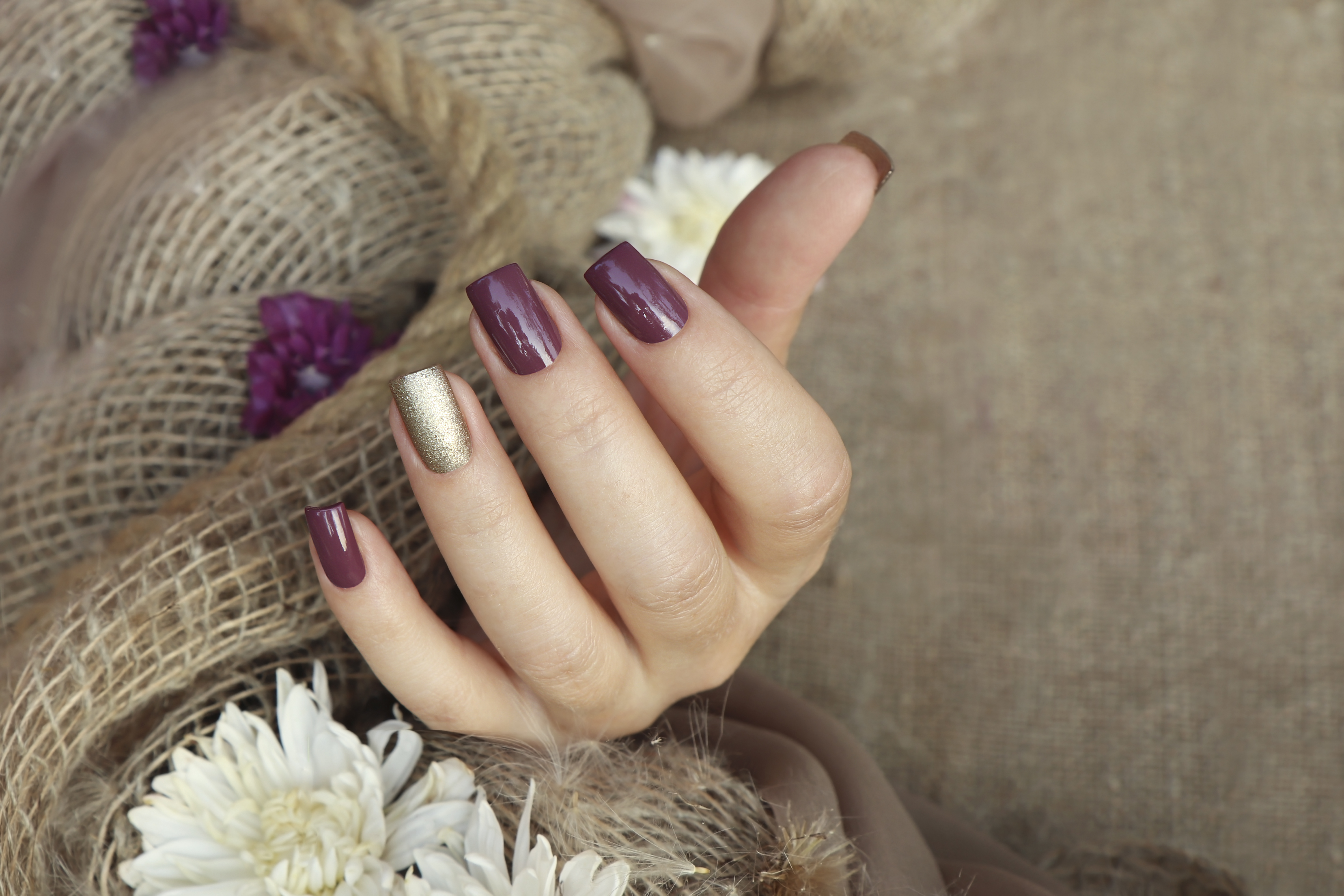 Eine weibliche Hand mit pflaumen- und goldfarbenen Nägeln | Quelle: Getty Images