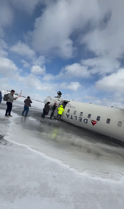 Weitere Passagiere verlassen das beschädigte Delta-Flugzeug auf dem schneebedeckten Boden, während andere bei der Evakuierung helfen | Quelle: Instagram.com/eggxit