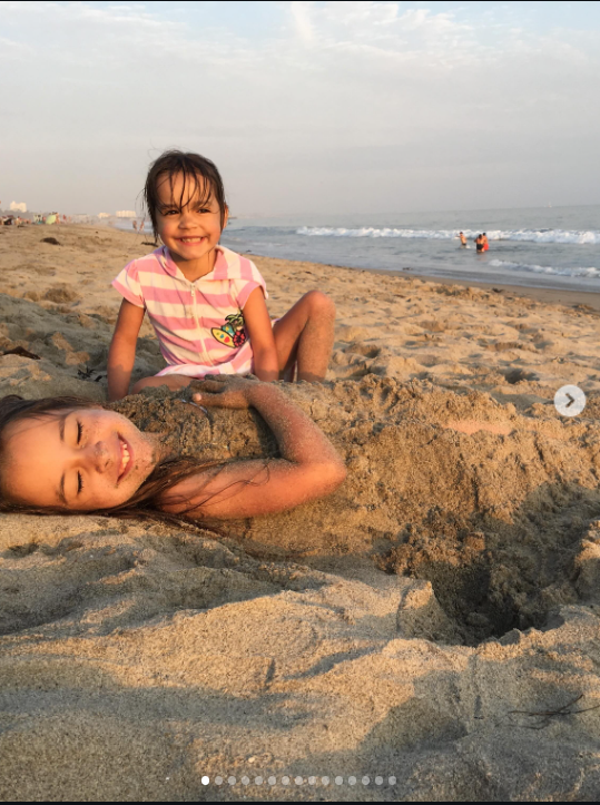 Mabel und Fiona sind als kleine Schwestern an einem sonnigen Strand zu sehen: Fiona steckt spielerisch im Sand, während Mabel hinter ihr lächelt. Dieser unbeschwerte Moment aus ihrer Kindheit hat nach Fionas Tod nun eine besonders bewegende Bedeutung. | Quelle: Instagram/mabellowe_