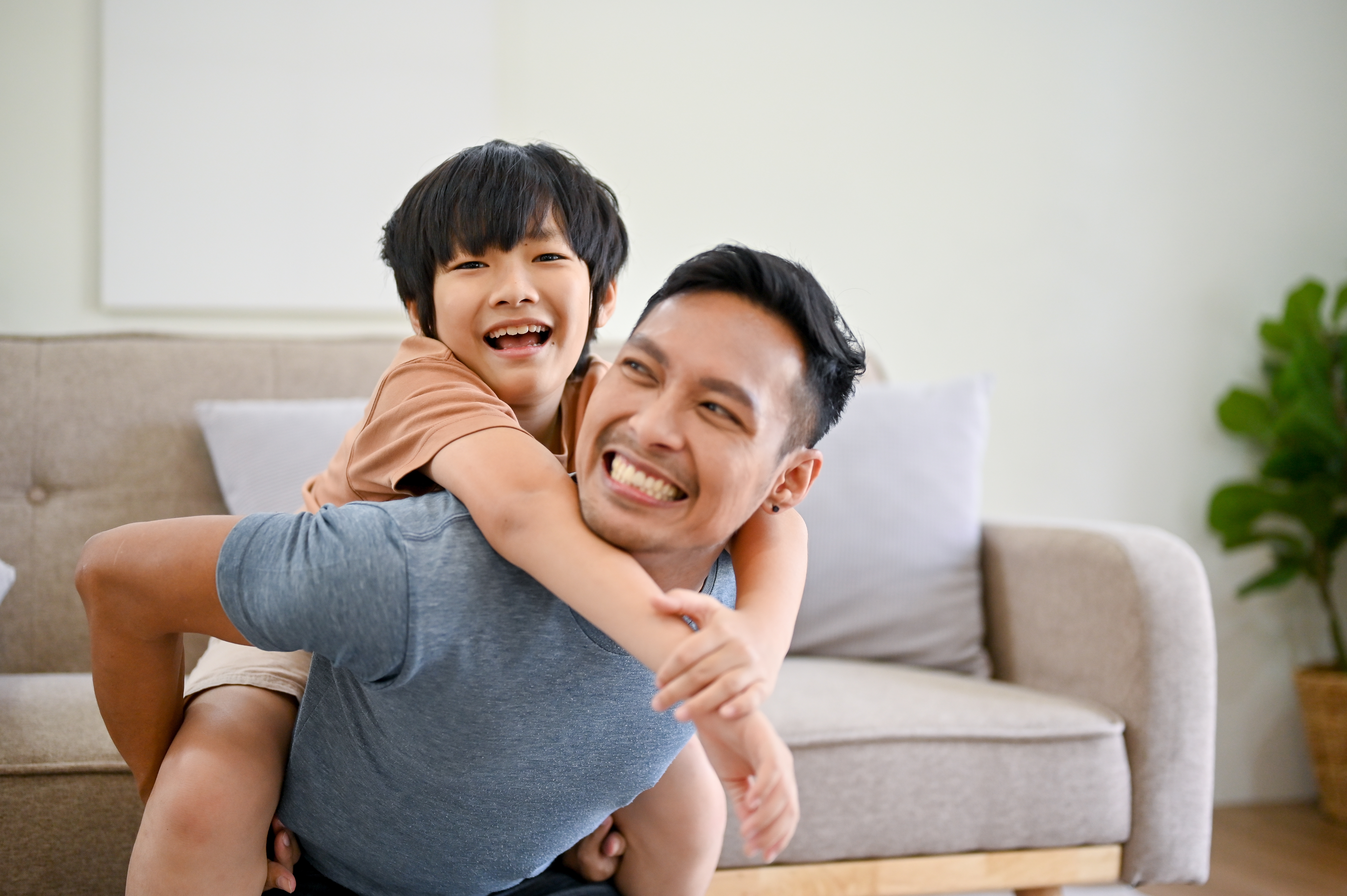 Asiatischer Sohn auf dem Rücken seines Vaters, lächelnd | Quelle: Shutterstock