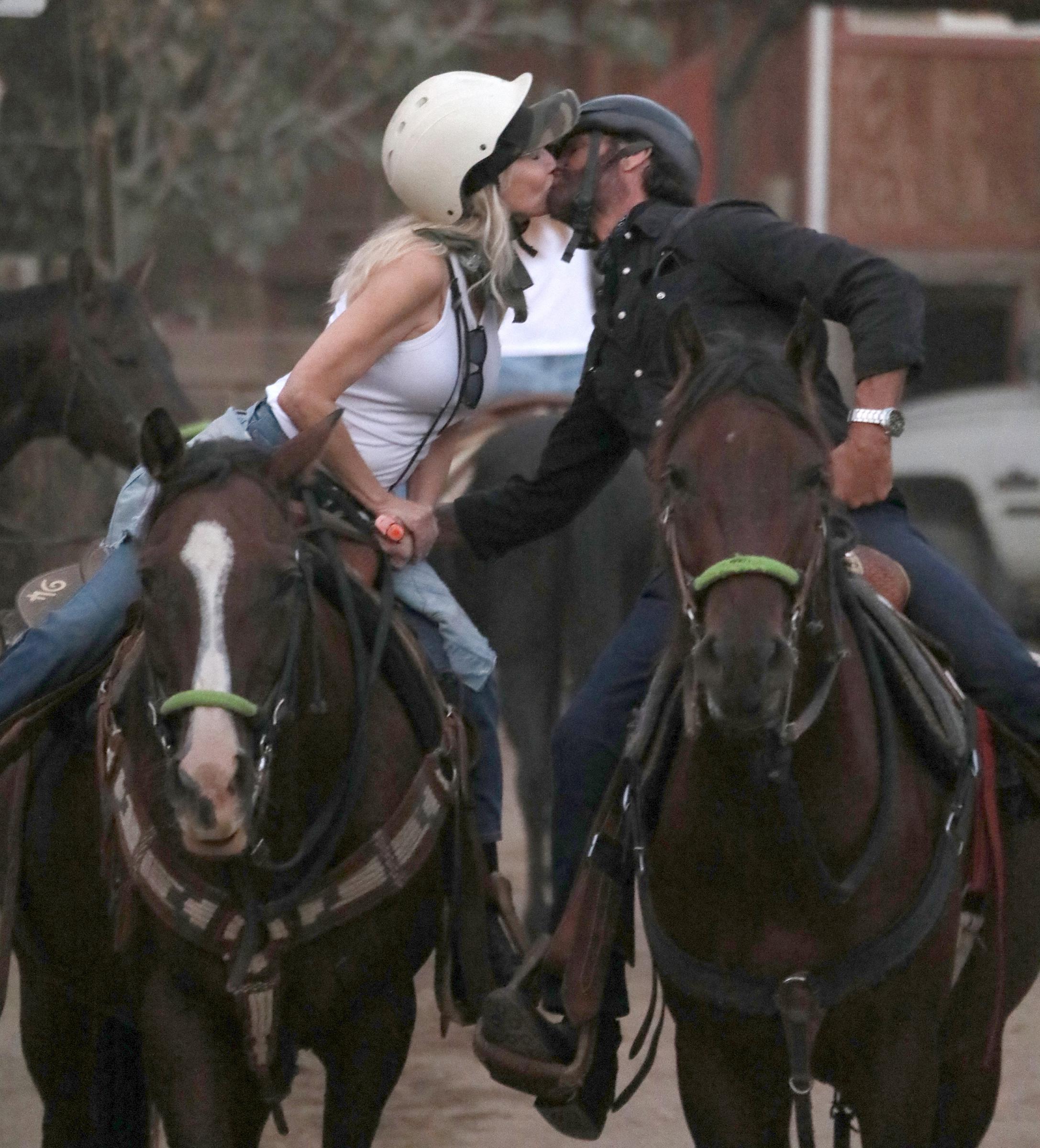 Heather Locklear und Lorenzo Lamas tauschen während eines Besuchs auf der Sunset Ranch in den Hollywood Hills am 22. September 2026 in Los Angeles, Kalifornien, einen zärtlichen Kuss auf dem Pferderücken aus. Locklear, die in Reithelmen und Jeans für den Ausritt gekleidet ist, trägt ein weißes Tanktop, während sie sich vorbeugt, um Lamas zu küssen, der ein schwarzes Hemd und eine Armbanduhr trägt. | Quelle: Getty Images