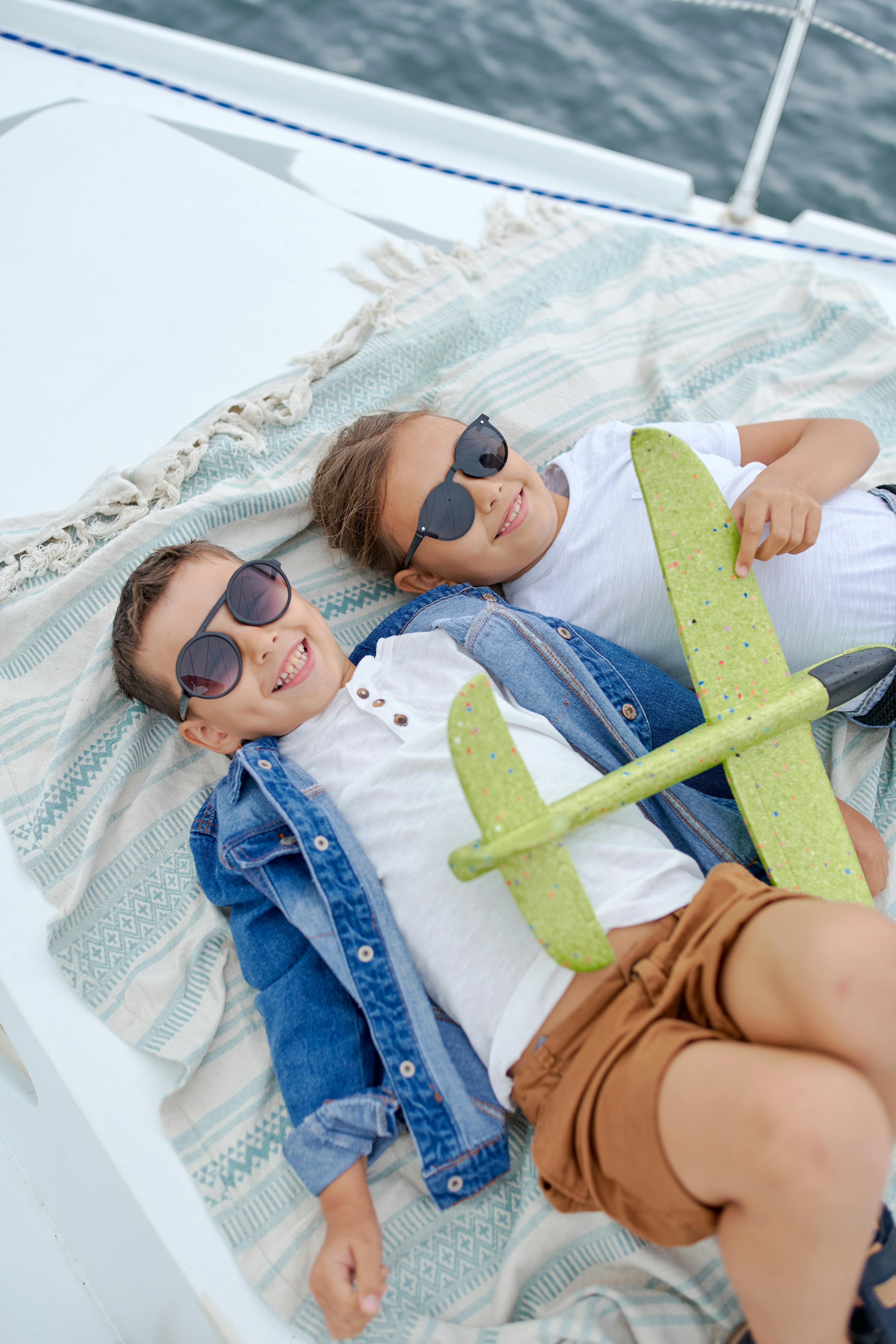 Zwei glückliche Kinder liegen mit dem Gesicht nach oben auf einem Boot und spielen mit einem Spielzeugflugzeug | Quelle: Pexels